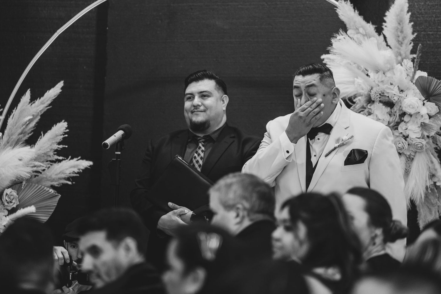 Black and white photo of wedding reception guests listening to speeches.