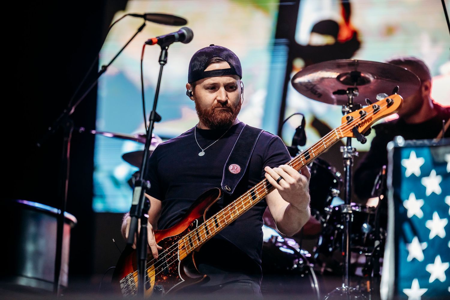 Bass guitarist performing on stage with American flag backdrop during concert.