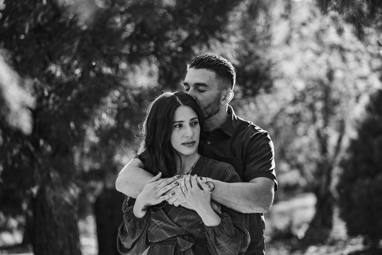 An intimate black and white portrait of a couple embracing outdoors.