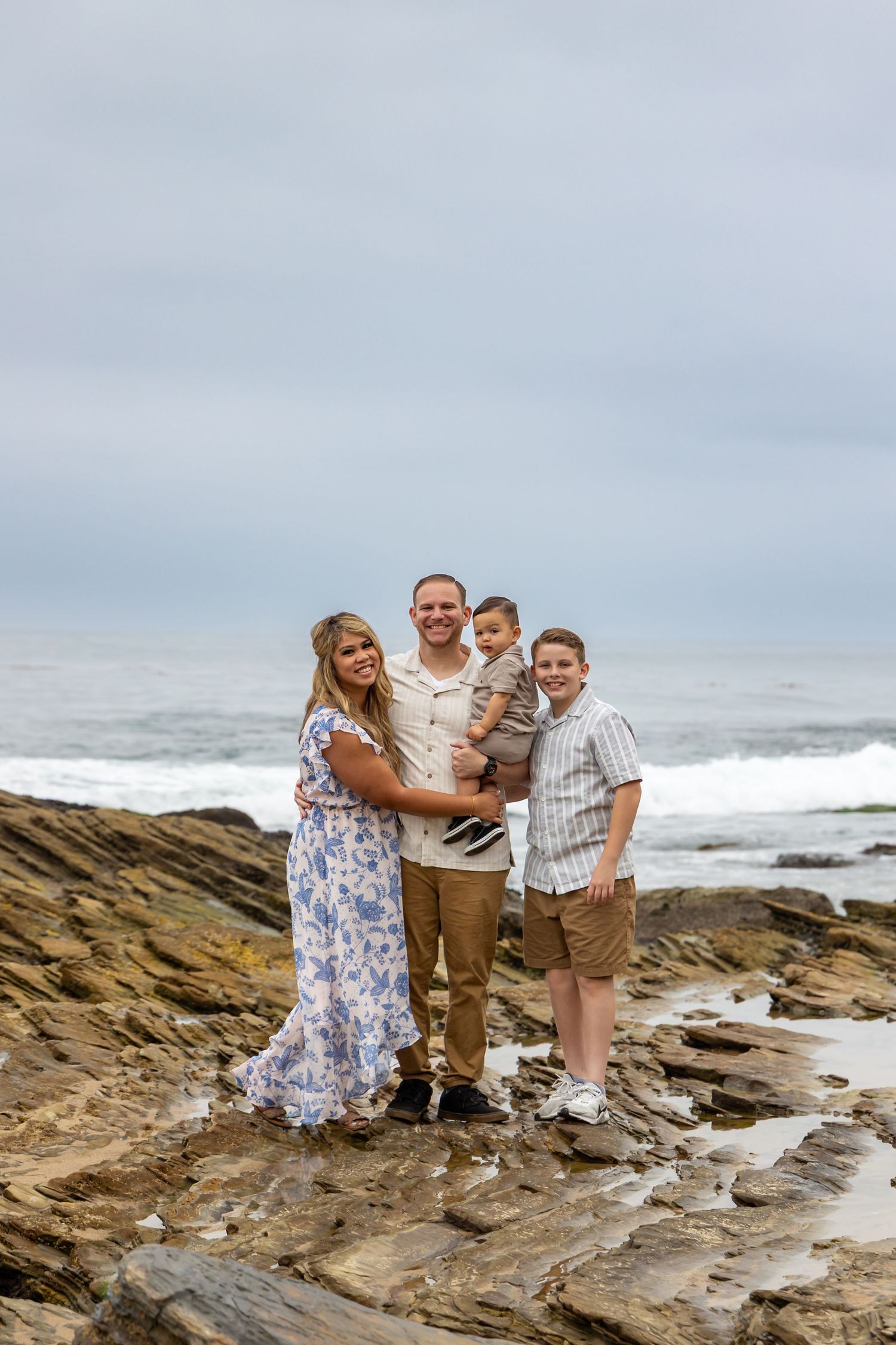 A family poses together on rocky coastal cliffs with ocean waves in the background.