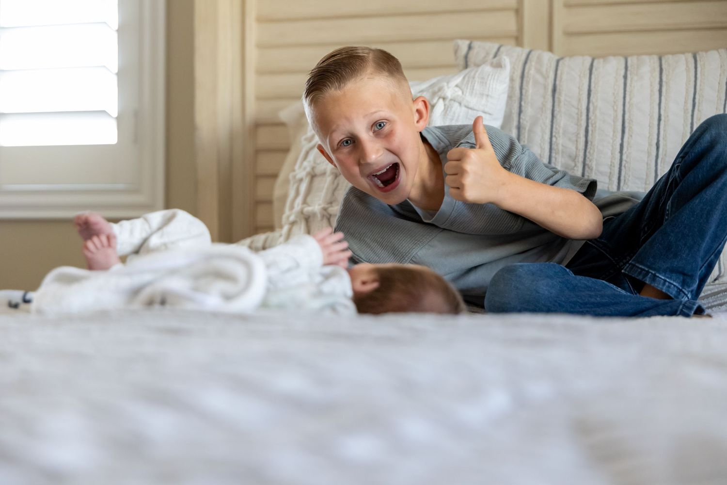 Young boy playing and making silly faces on bed with gray bedding.