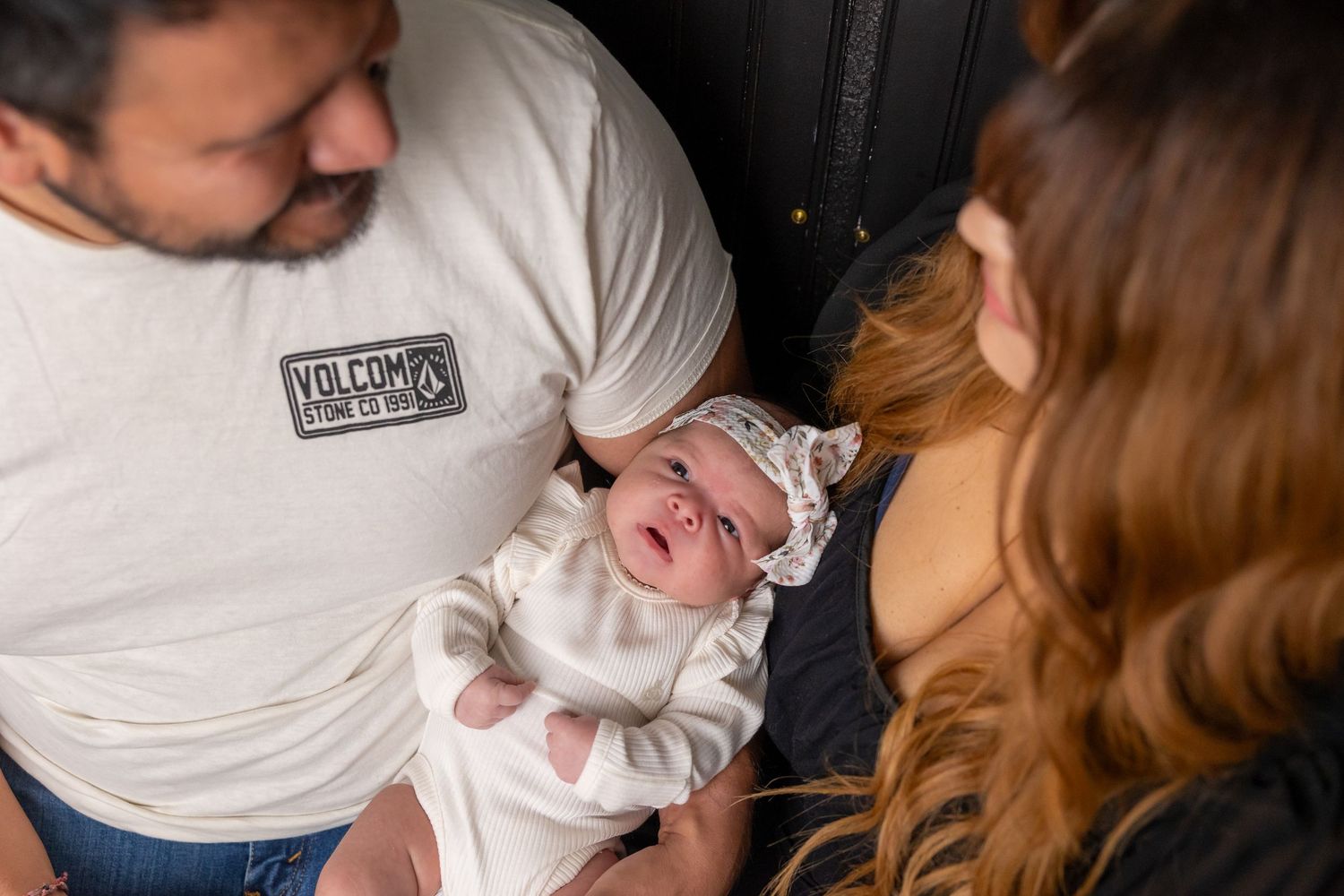 Newborn baby wearing white outfit held by parents during intimate moment.