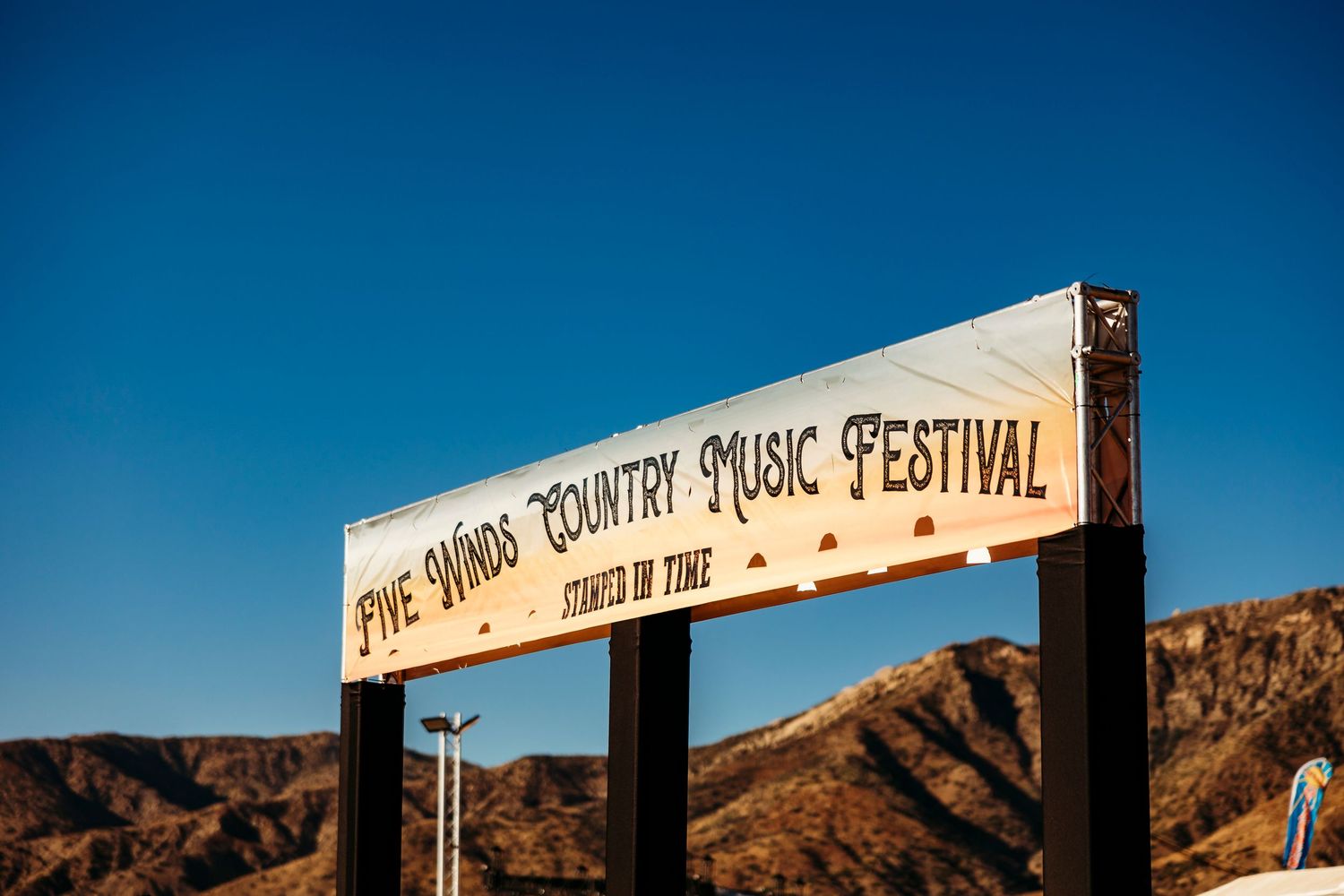 Wooden sign for 'Five Hands Country Music Festival' against blue desert sky and mountains.
