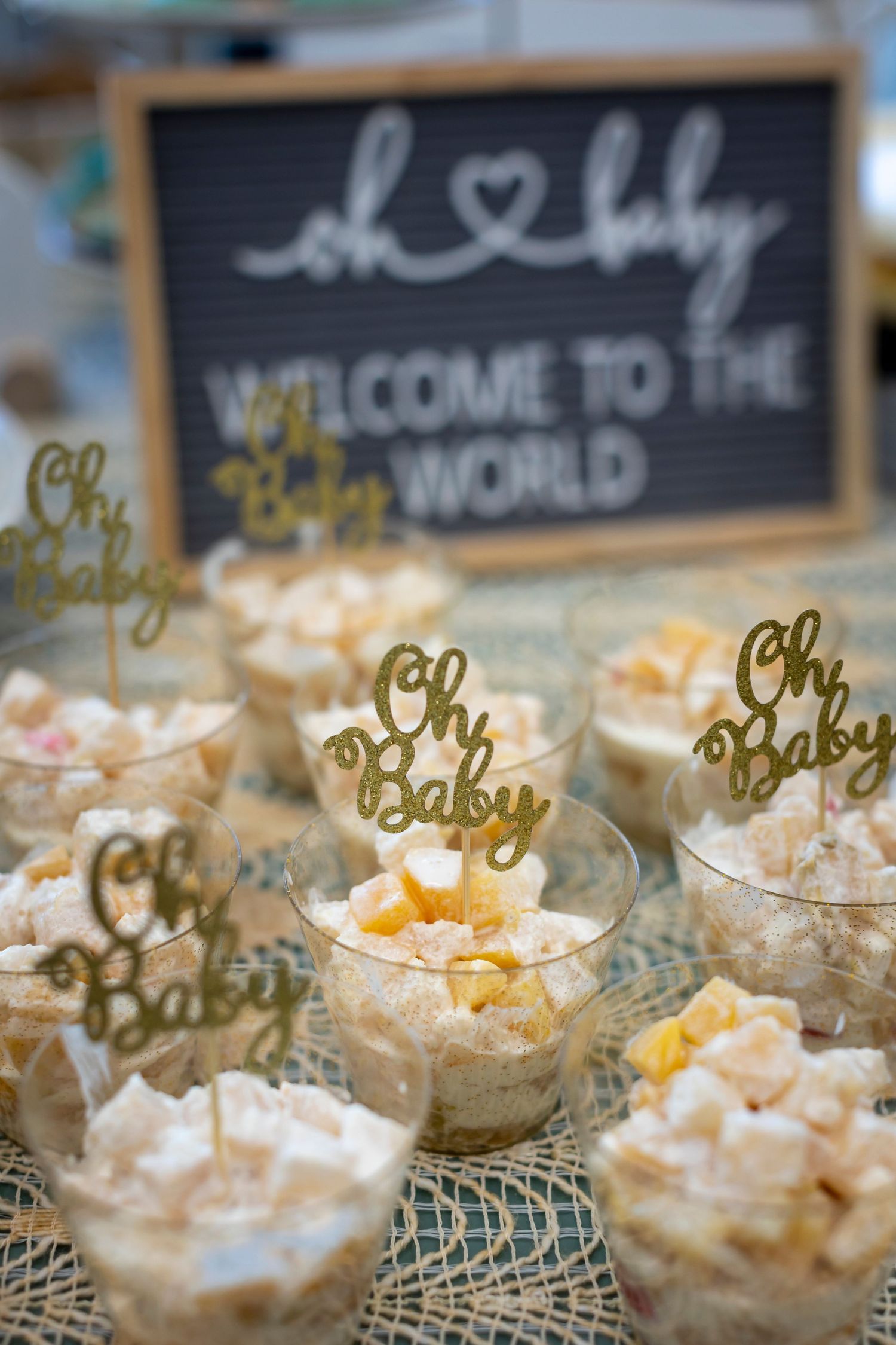 Elegant dessert display featuring small treats with gold 'Oh Baby' toppers and chalkboard signage.