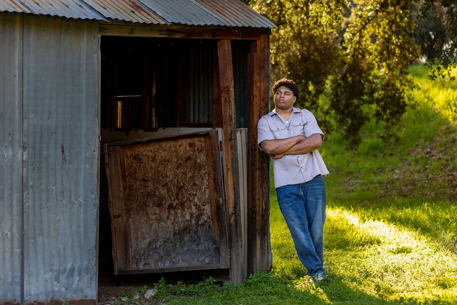 Someone leans against a rustic wooden shed in casual attire during golden hour in Yucaipa.