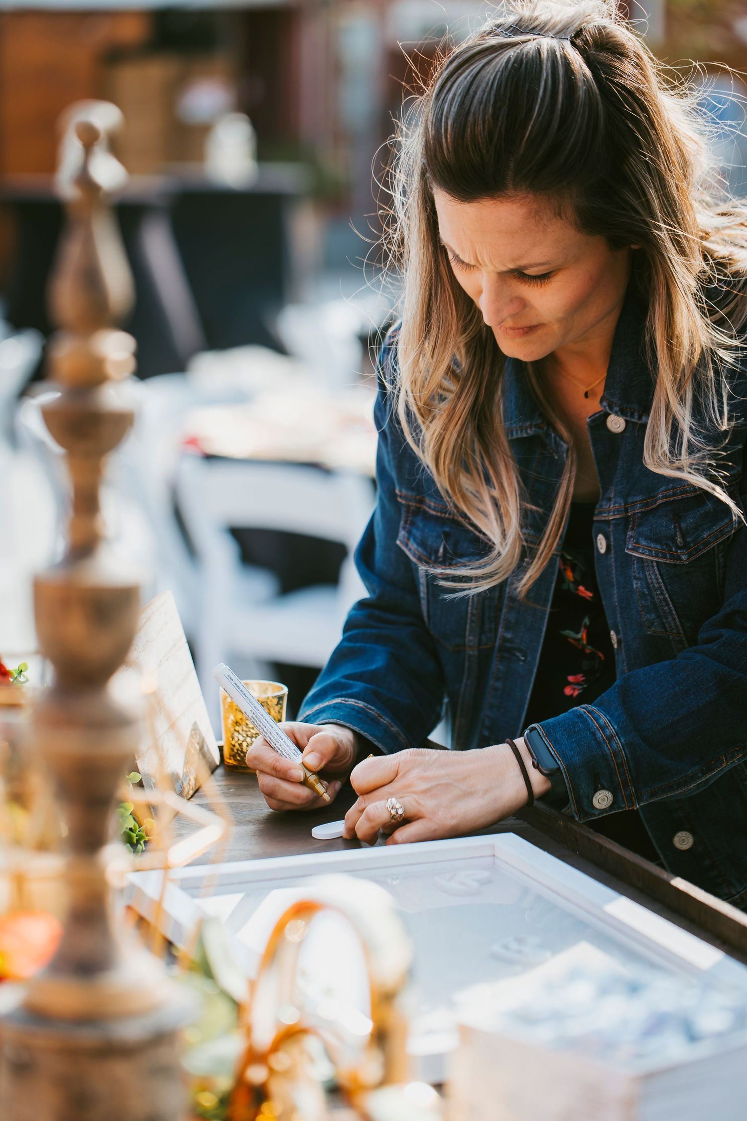 Wedding planner in denim jacket writing notes at outdoor event setup.