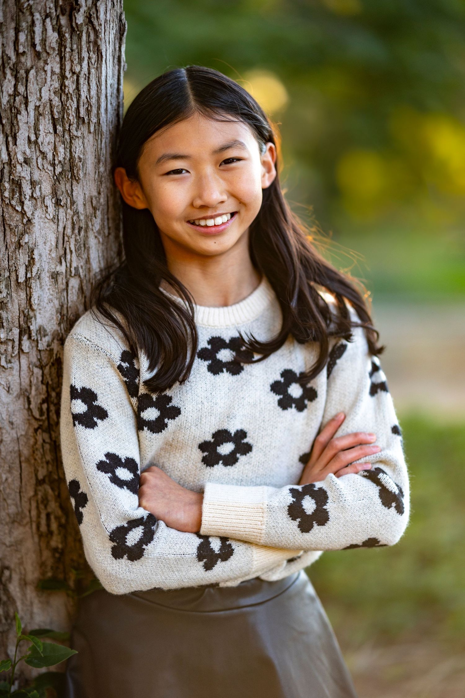 Person in floral sweater poses against tree trunk in autumn outdoor setting.