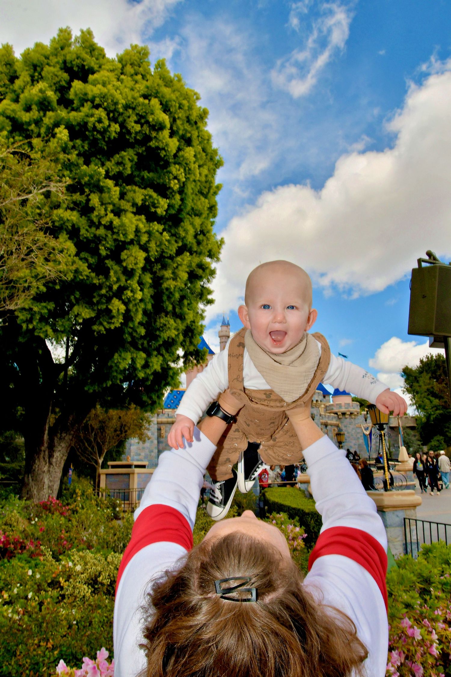 Parent playfully lifting and holding a small child against a blue sky with trees in the background.
