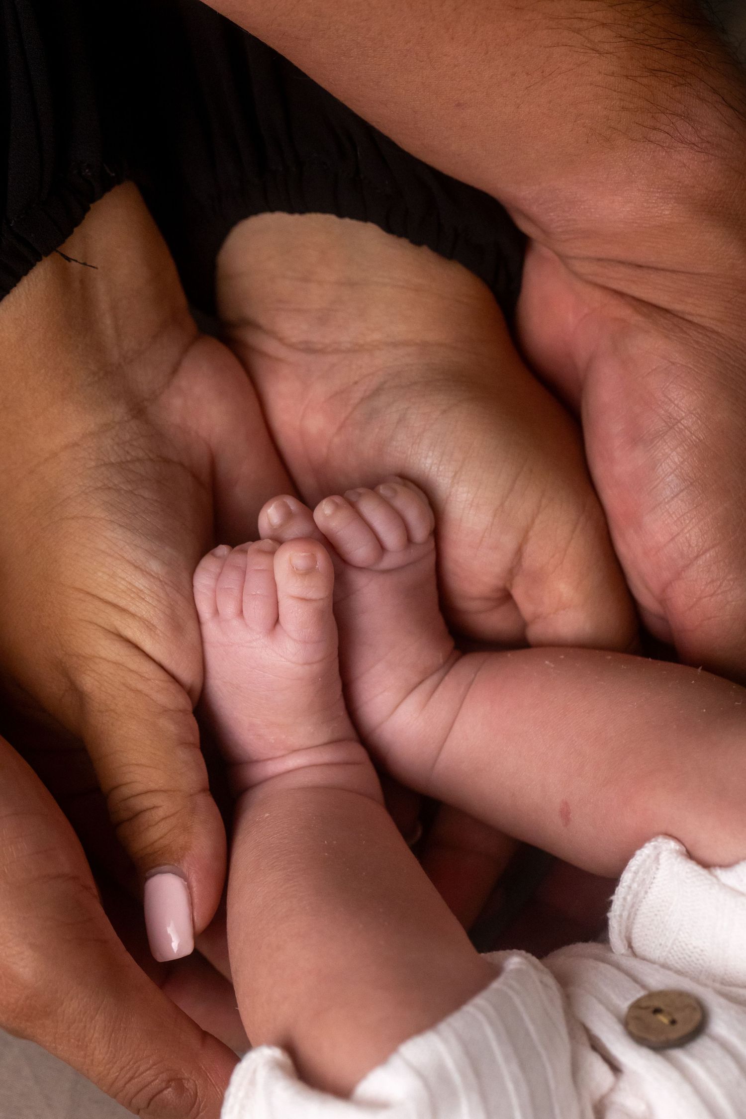 Close-up view of adult hands interacting with a small baby's fingers in a tender moment.