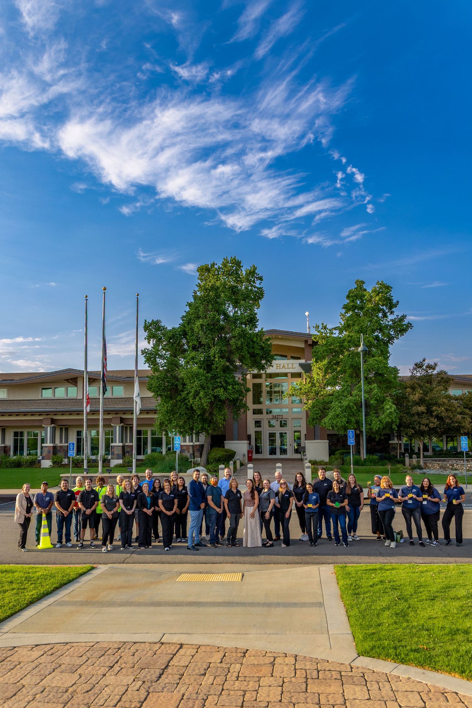 Large group gathered outdoors under blue sky for a formal ceremony in front of a modern building.