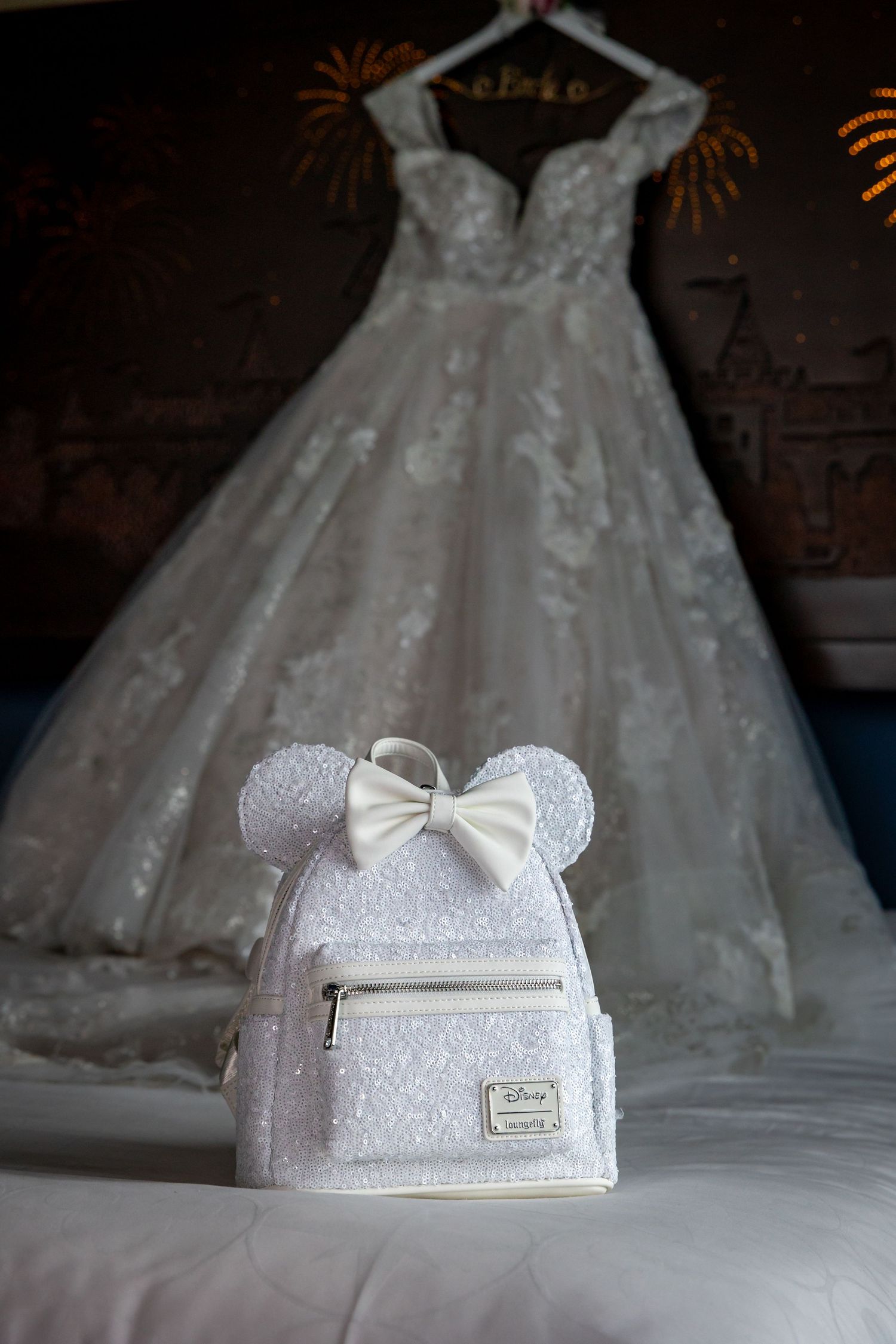 A white Disney-themed Minnie Mouse bridal purse with bow detail displayed near a wedding dress.