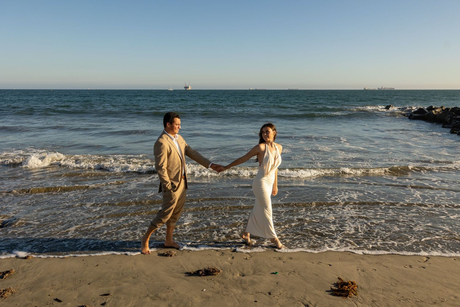 A couple walks along the shoreline as waves crash on a sunny beach.