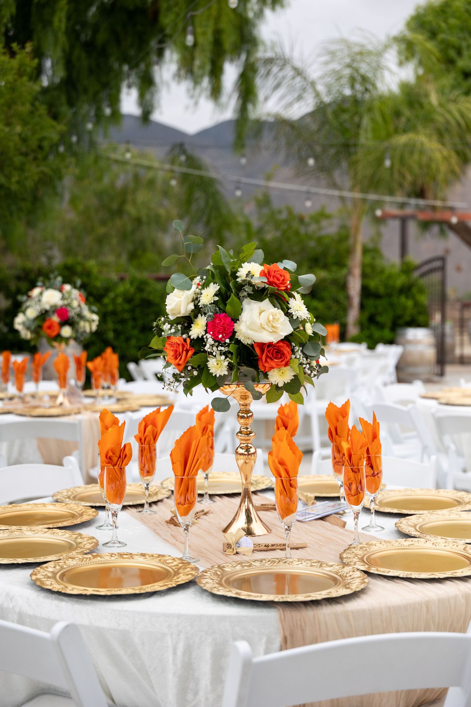 Elegant table settings with orange and floral centerpieces at outdoor celebration.