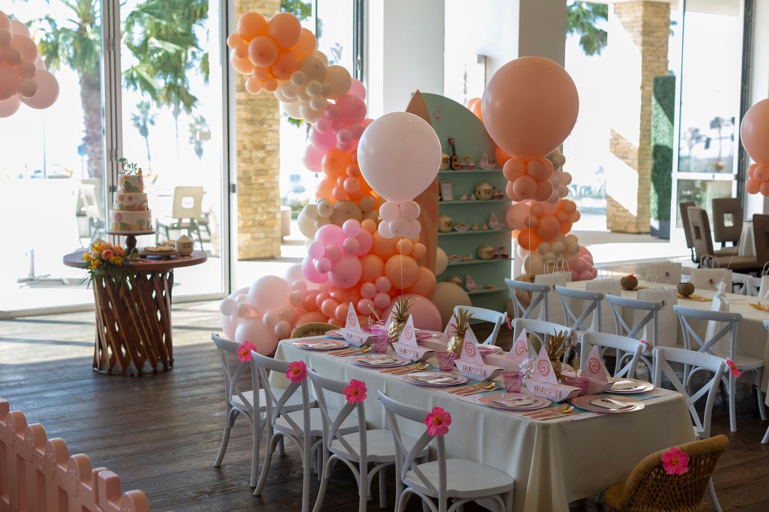 Event space decorated with white chairs, pink accents, and orange and white balloon arrangements in Huntington Beach.