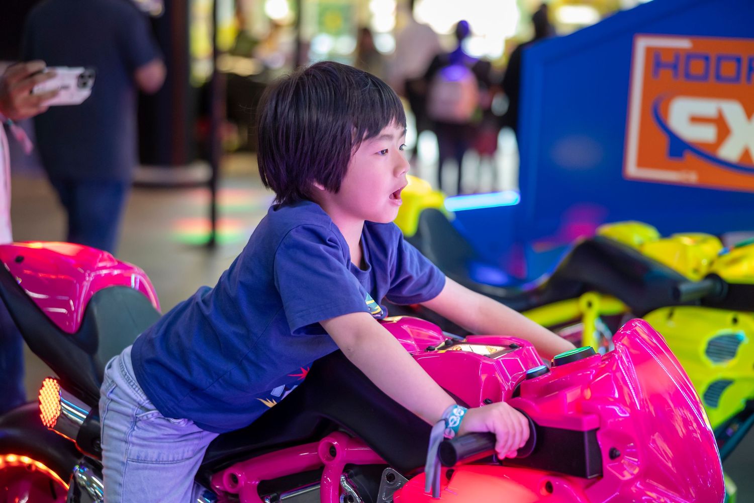 Children riding on pink play equipment in an indoor entertainment center.