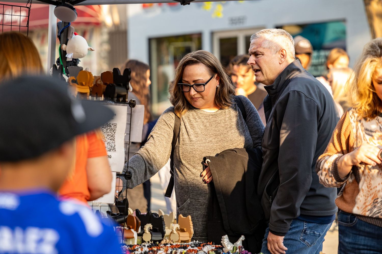 Shoppers browsing vendor displays at an outdoor market or festival.