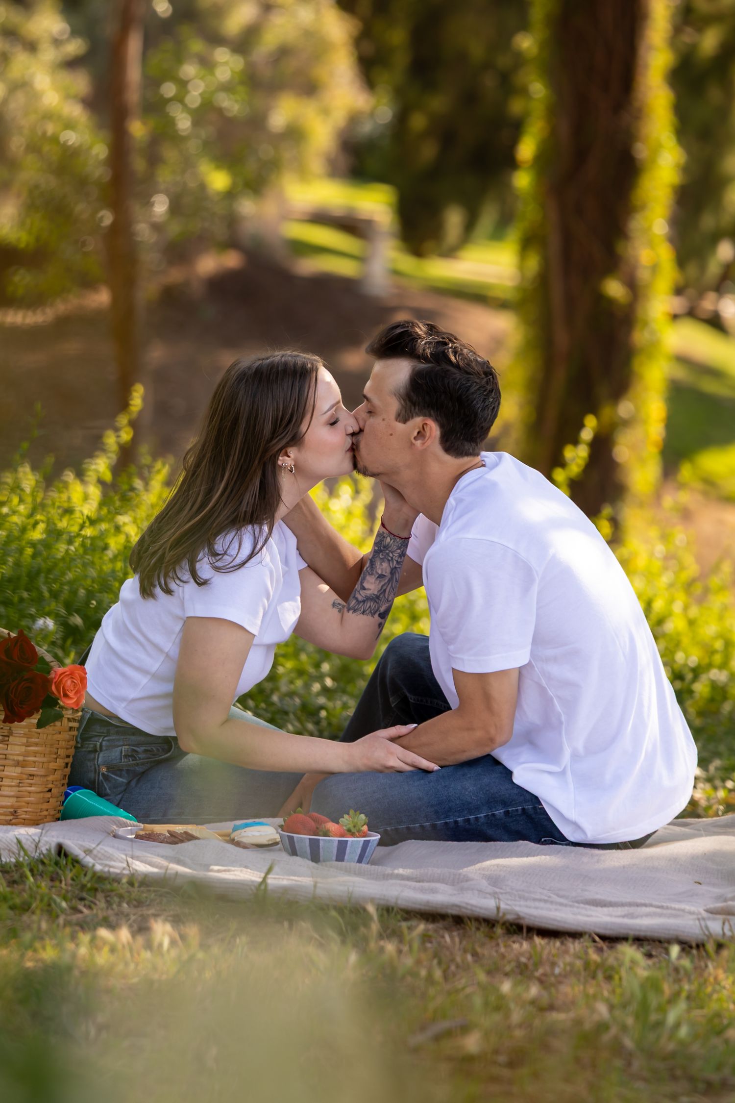 A romantic summer picnic scene in a sunlit park with a couple sharing a tender moment on a blanket in Redlands.
