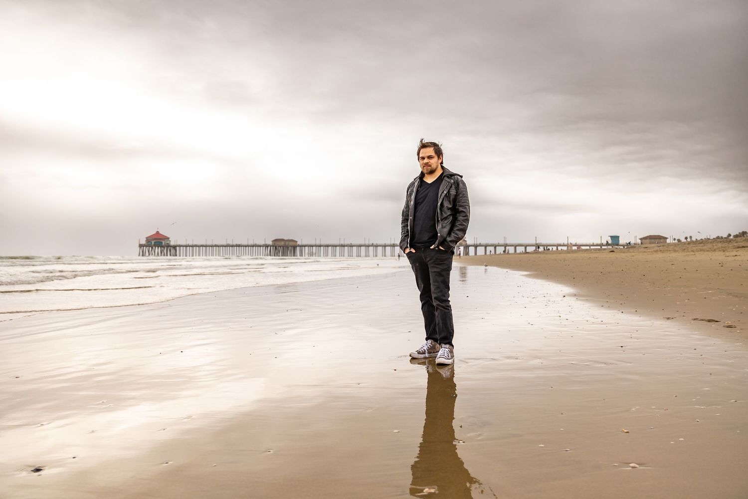 Person in black attire walks along a misty beach with a pier visible in the distance in Huntington Beach.