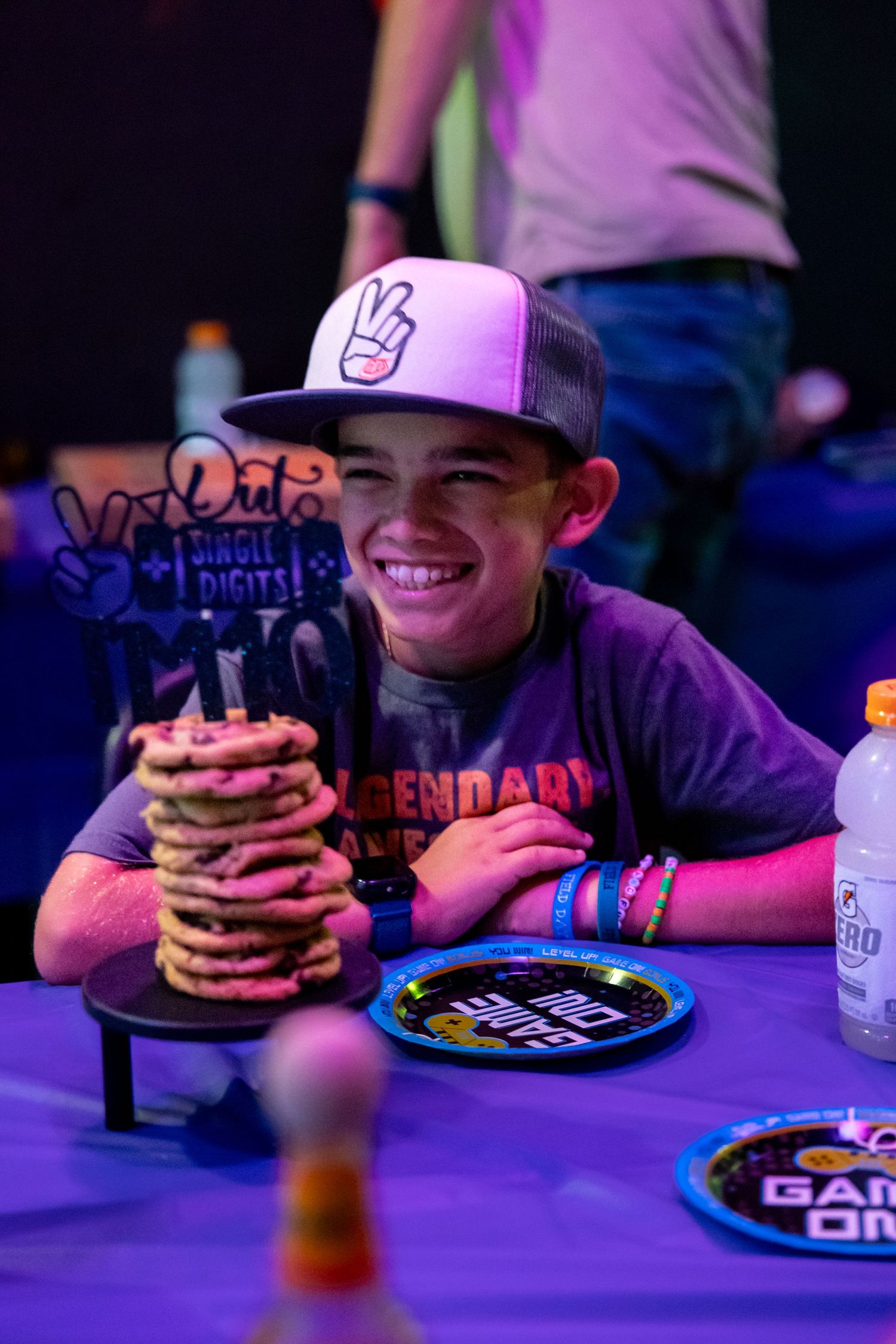 Someone enjoys a large stack of pancakes under purple arcade lighting.