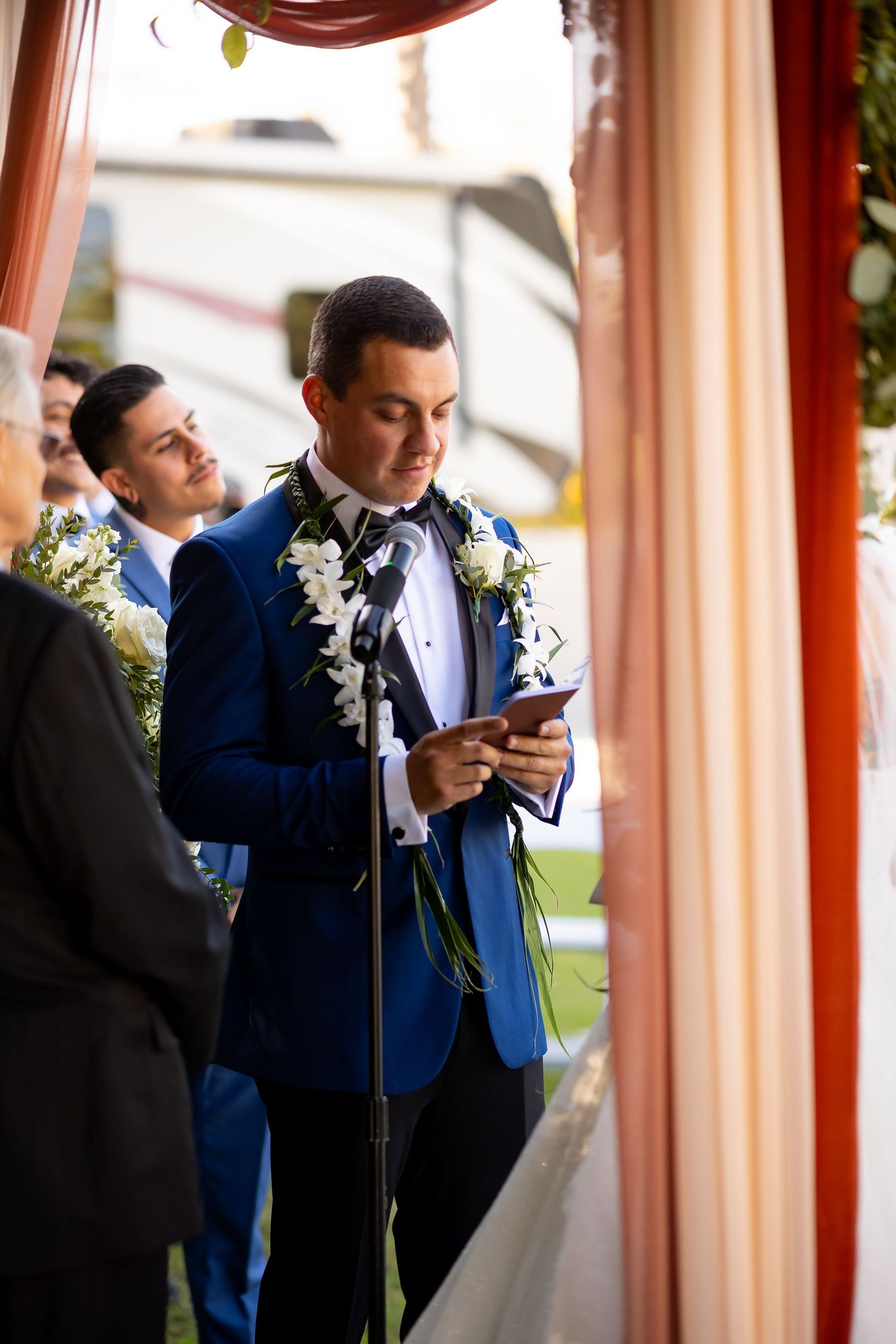 Groomsmen in blue blazers and black suits checking their phones during a wedding ceremony.
