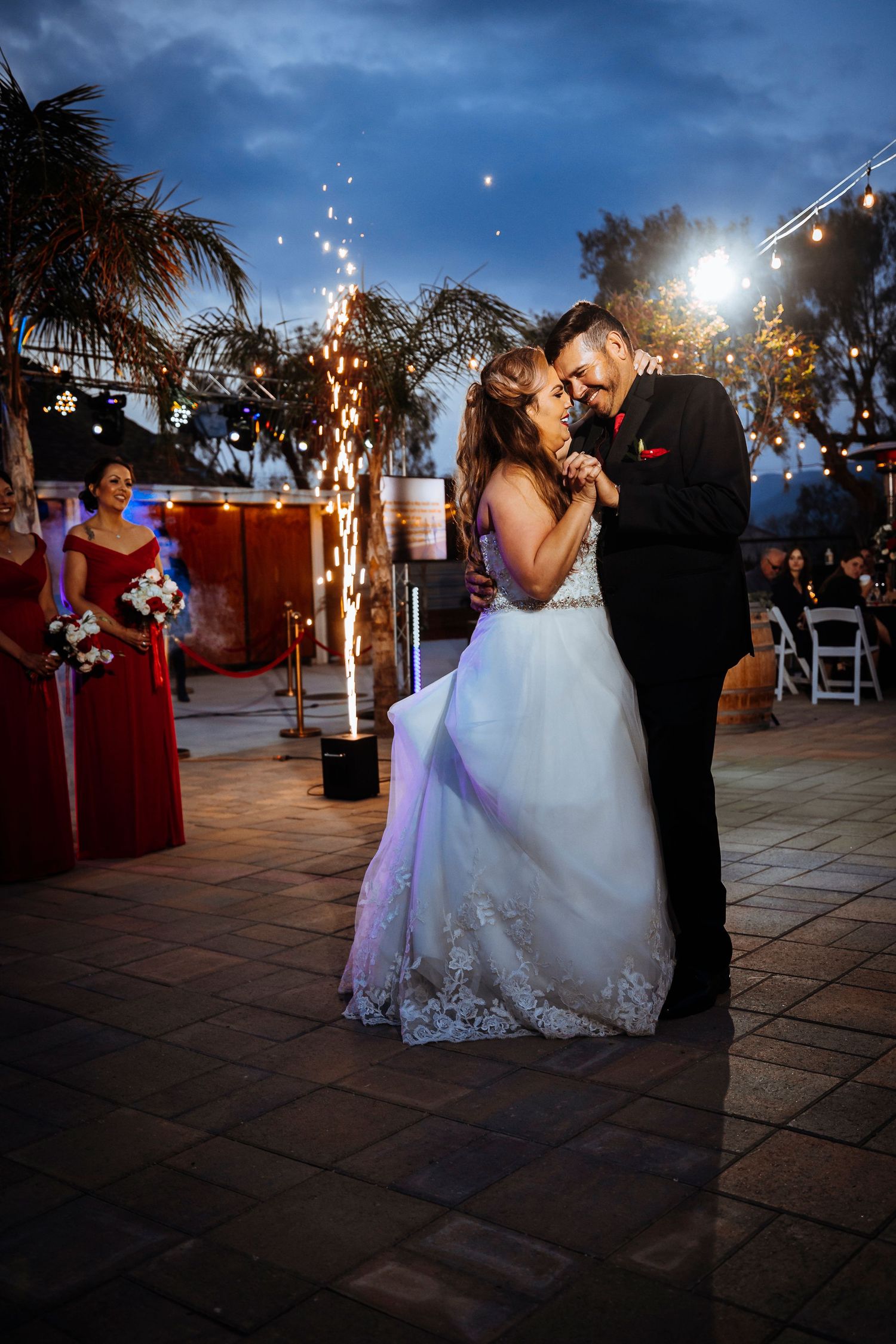Couple shares first dance under twinkling lights and sparklers at outdoor evening reception.