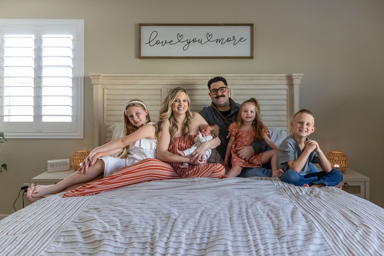 Family relaxing together on bed with striped bedding under 'love grows here' sign in Beaumont.