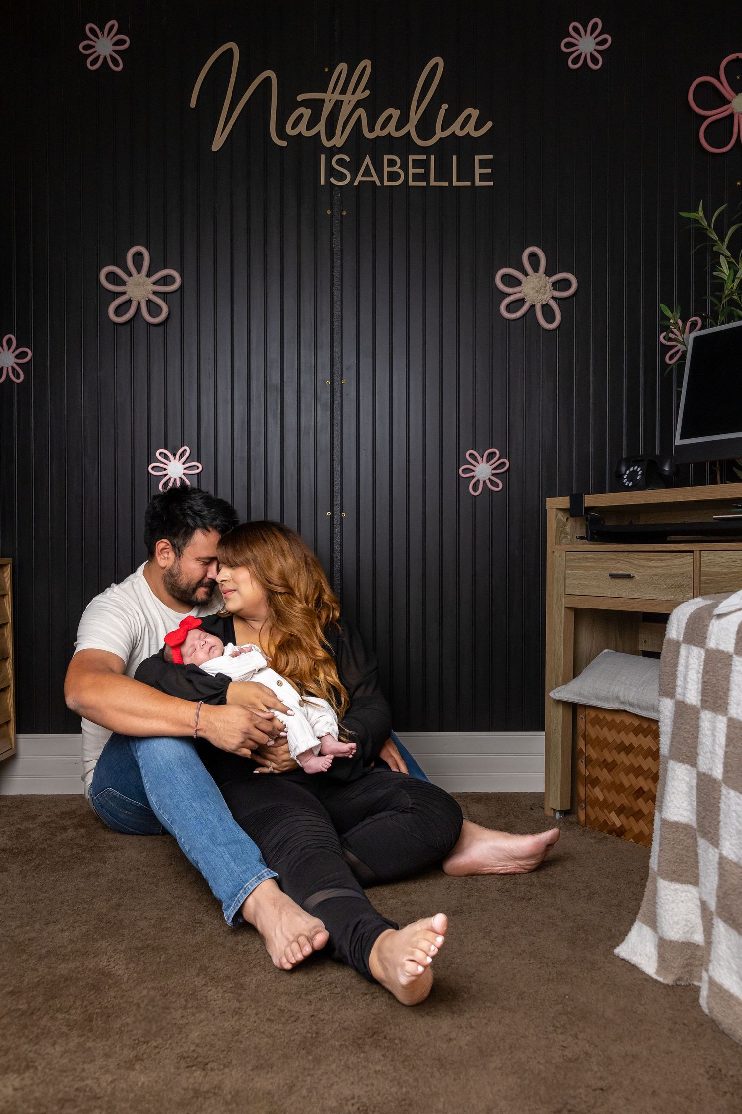 Family sitting on floor together in nursery with black accent wall and floral decorations.