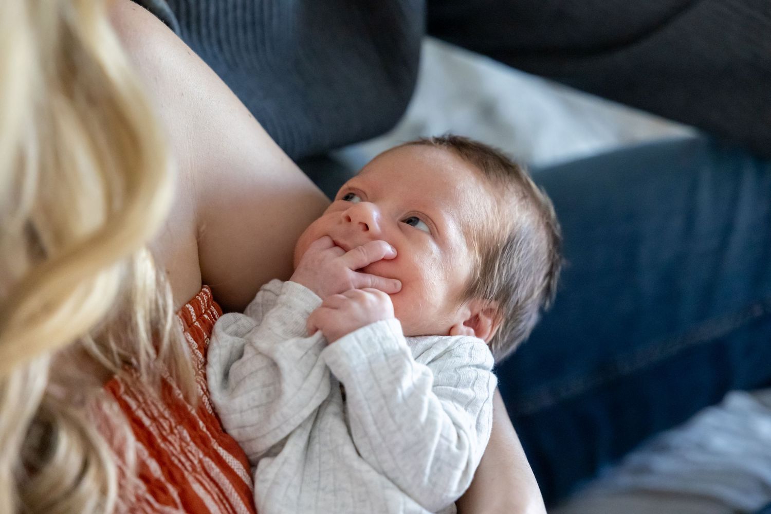 A newborn baby in a white onesie smiles while being cradled.