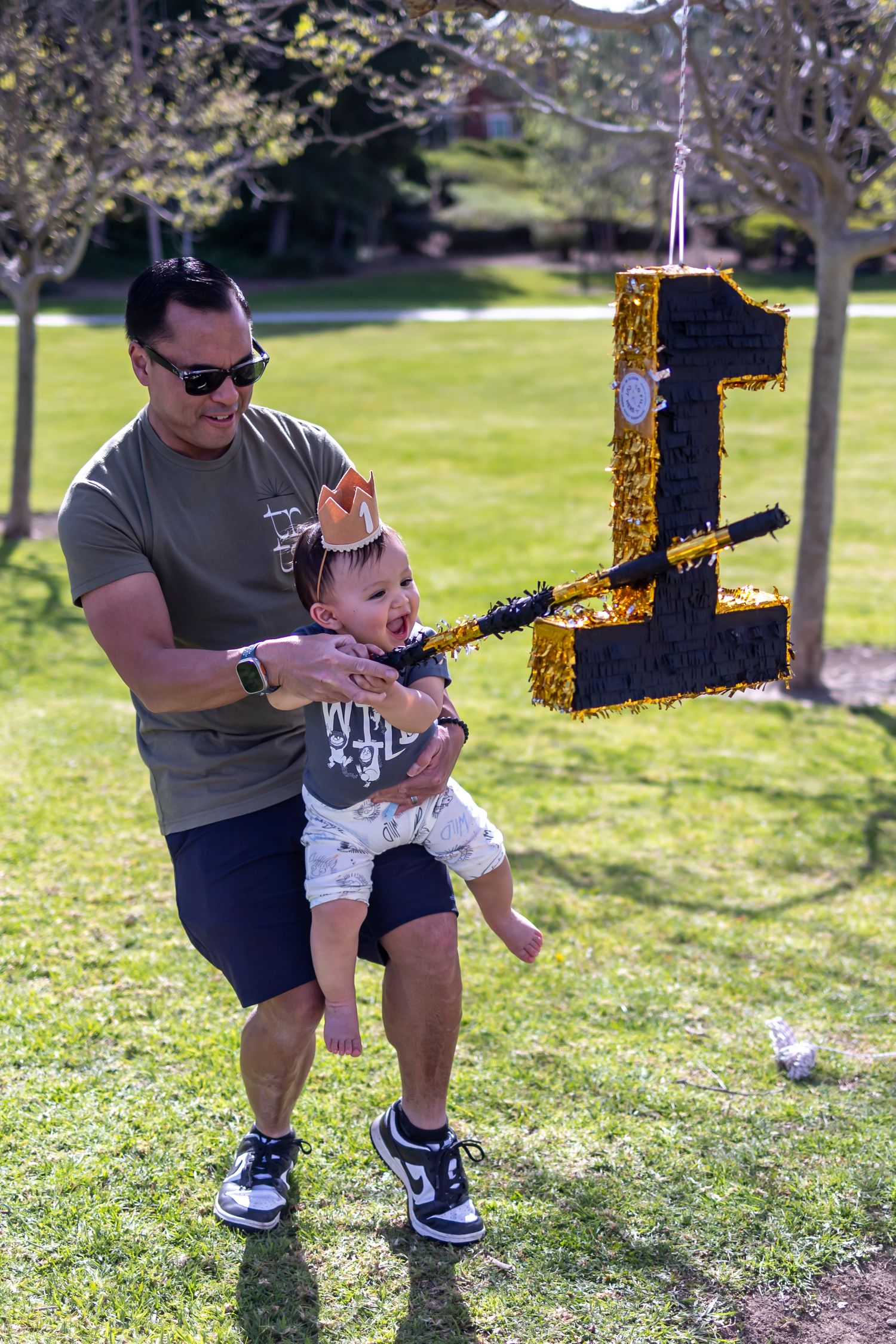Child reaching for golden number one pinata at outdoor party.