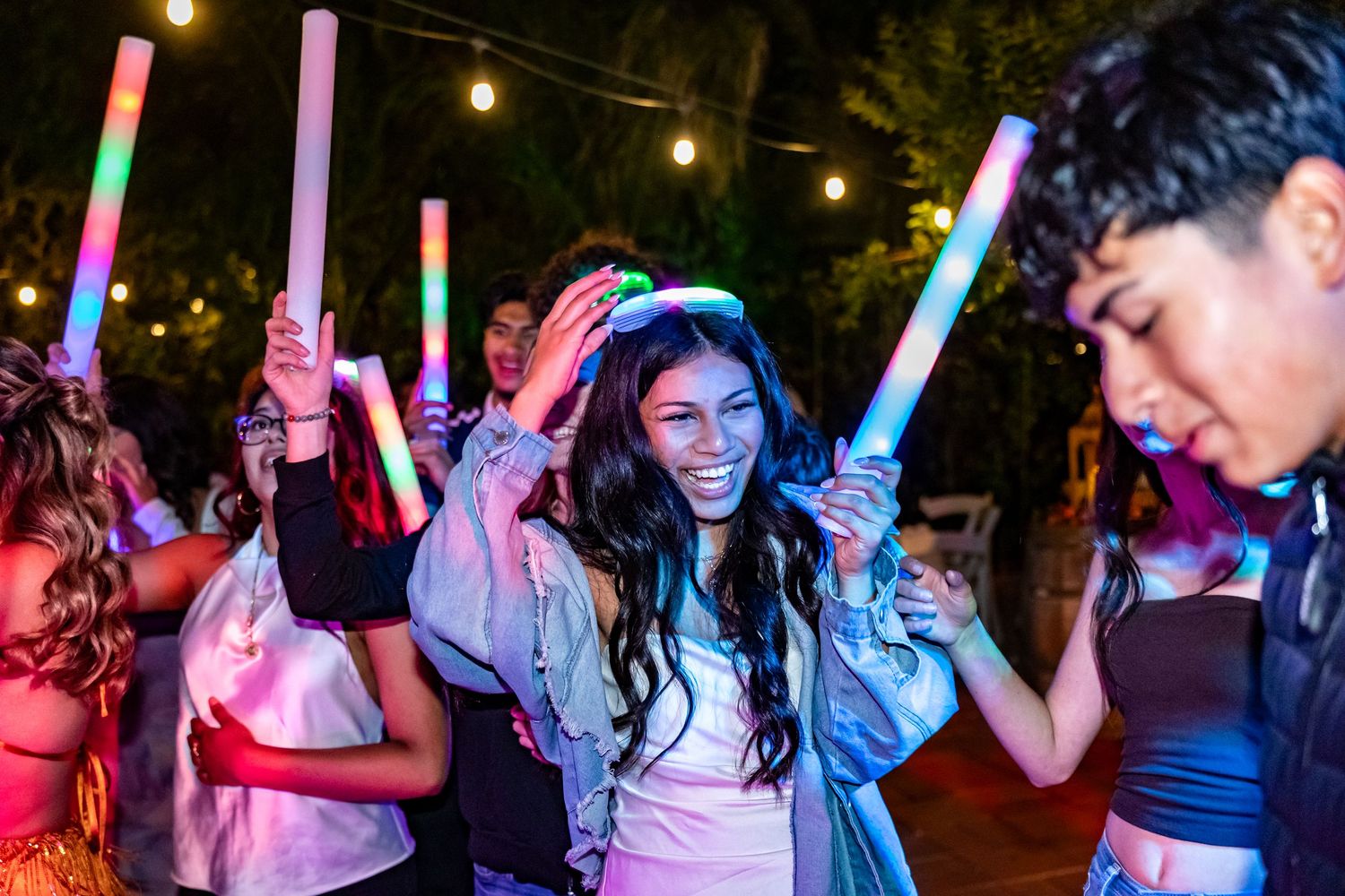 People waving light-up sticks while dancing at a nighttime outdoor celebration.