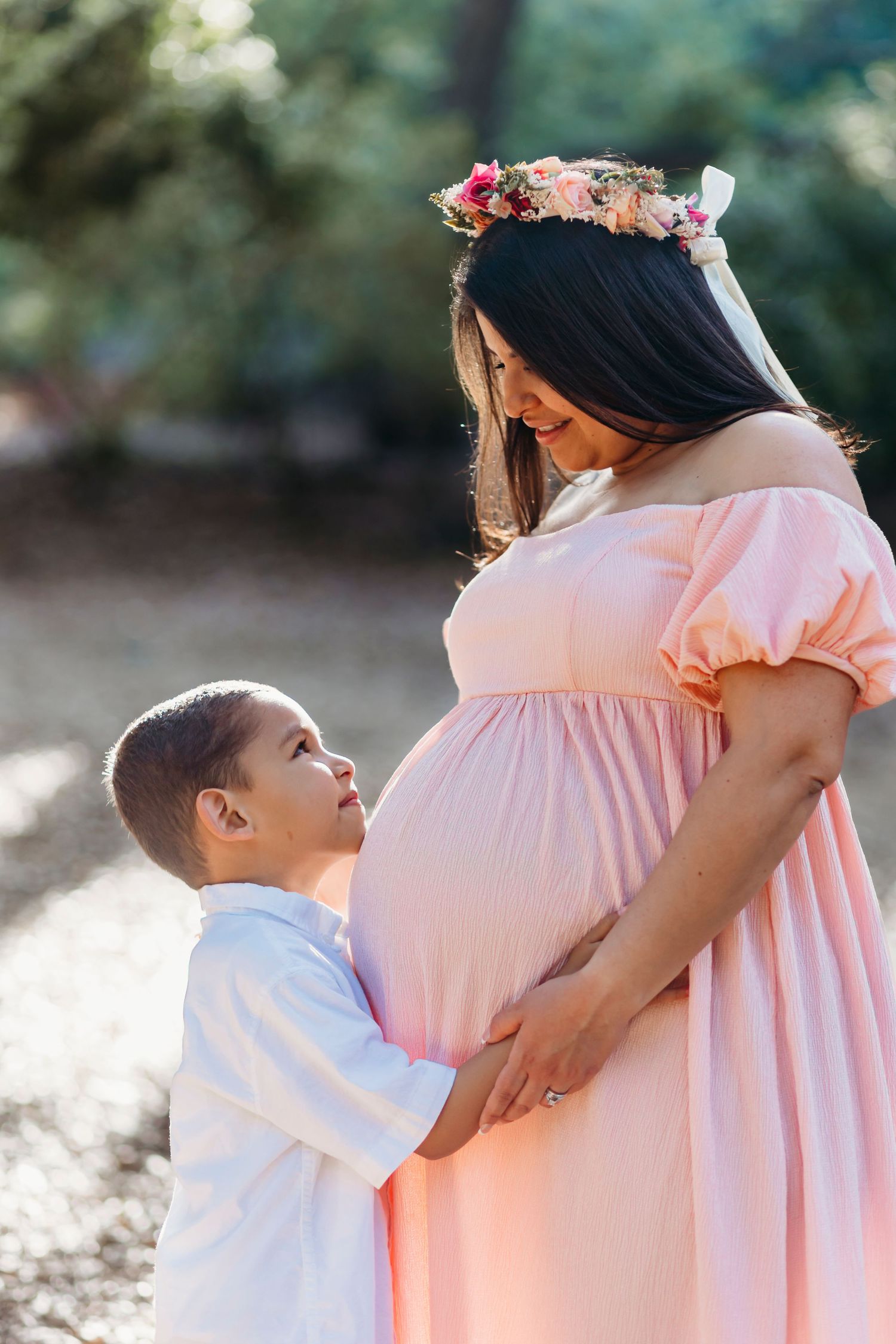 A tender maternal moment captured in soft lighting with a pink dress and floral crown.