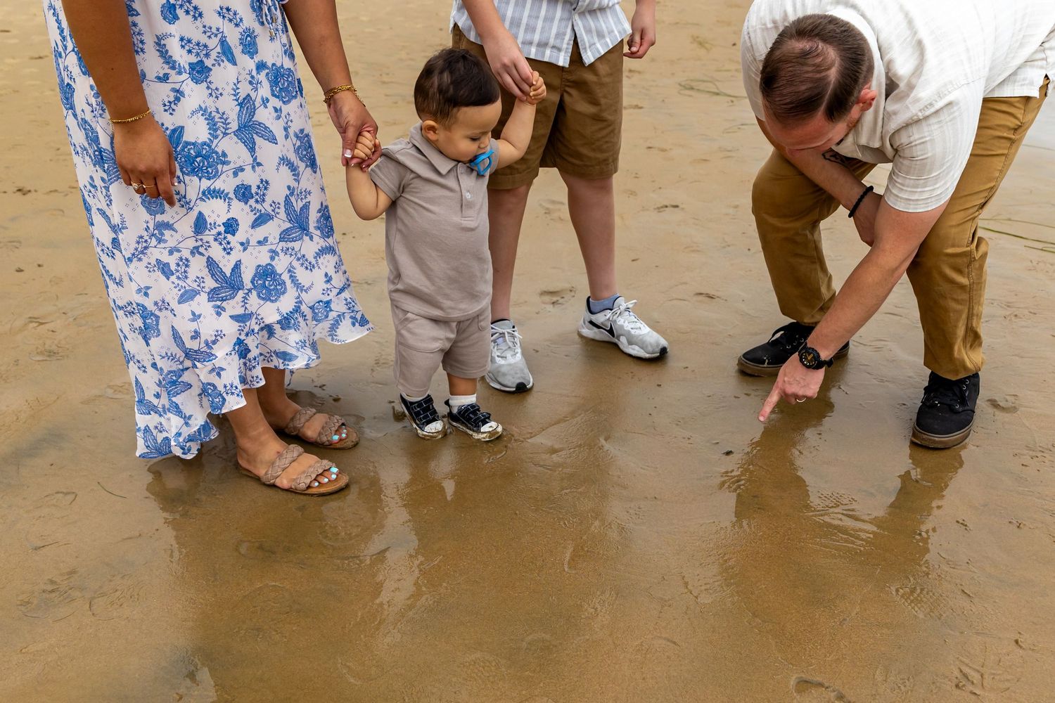 Family members examining something interesting in wet sand at the beach.