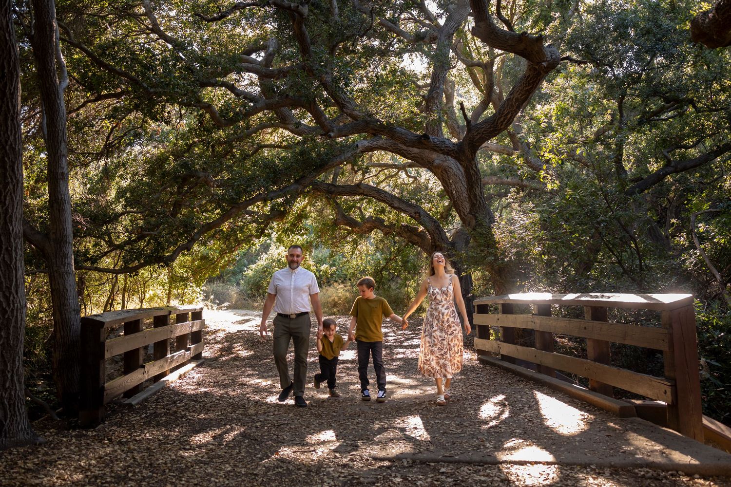 Family enjoying natural setting beneath large tree branches during outdoor photo shoot.