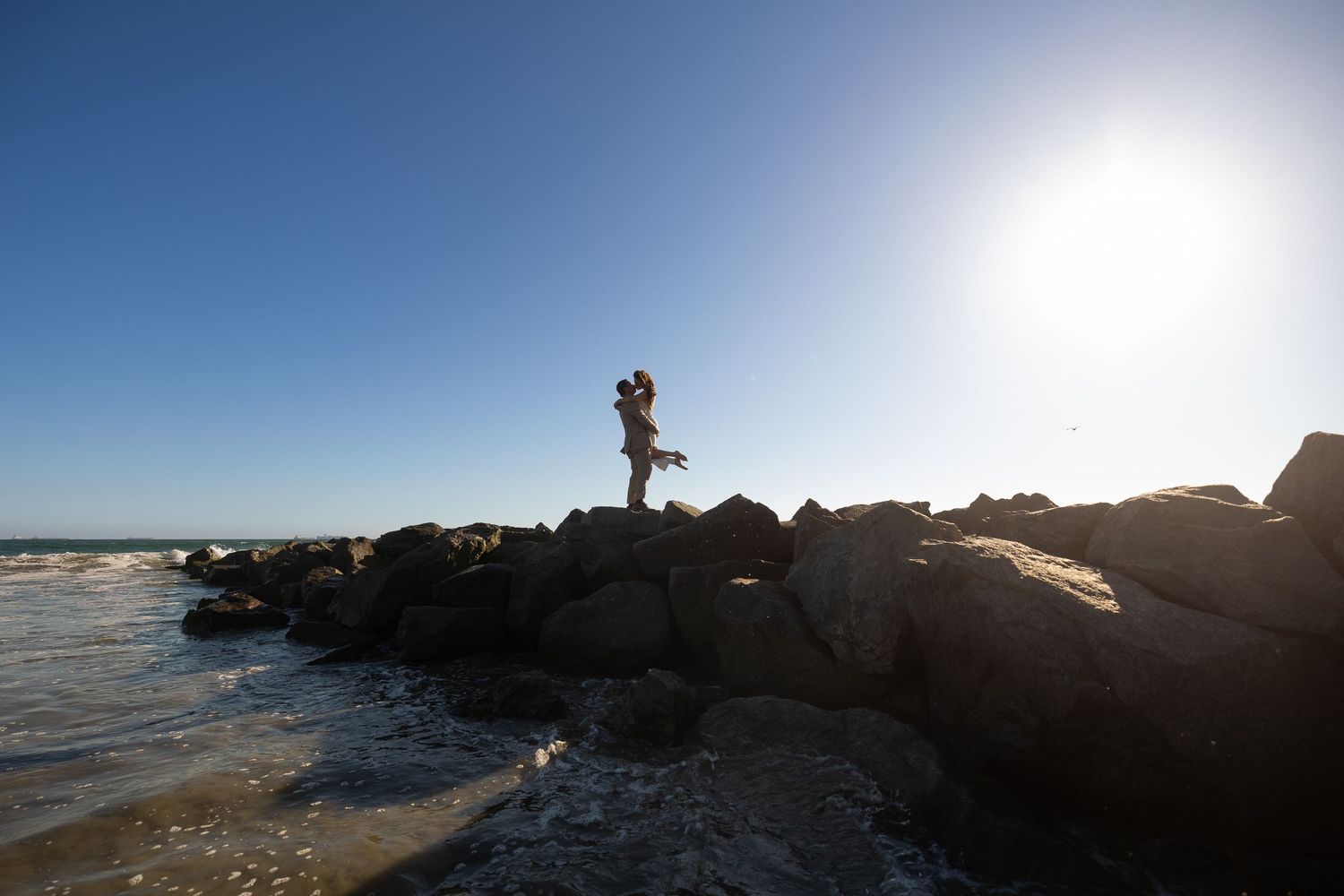 Dramatic coastal sunset silhouette with rocky shoreline and ocean waves.