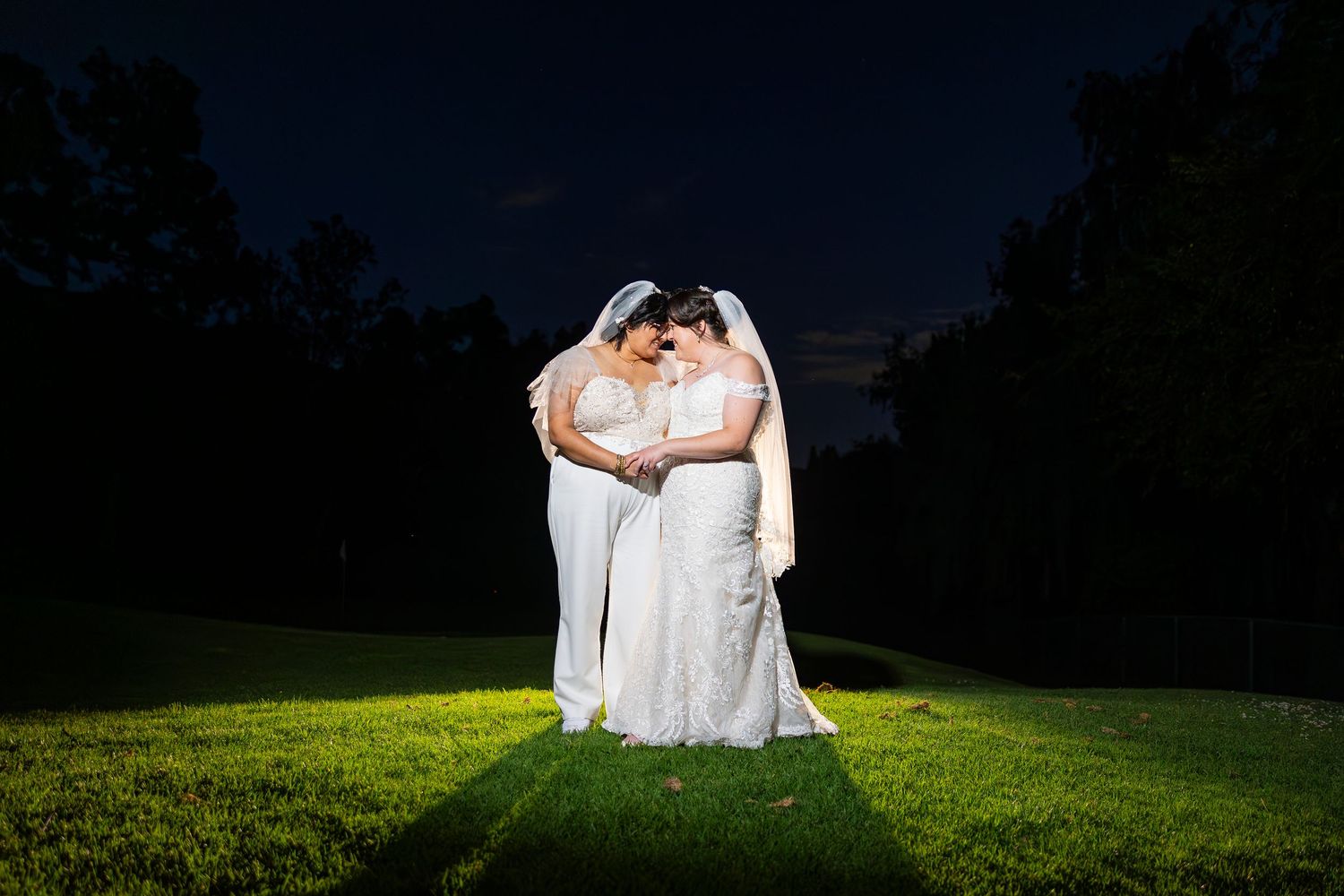 Dramatic night photography of two people in white dresses on illuminated grass.
