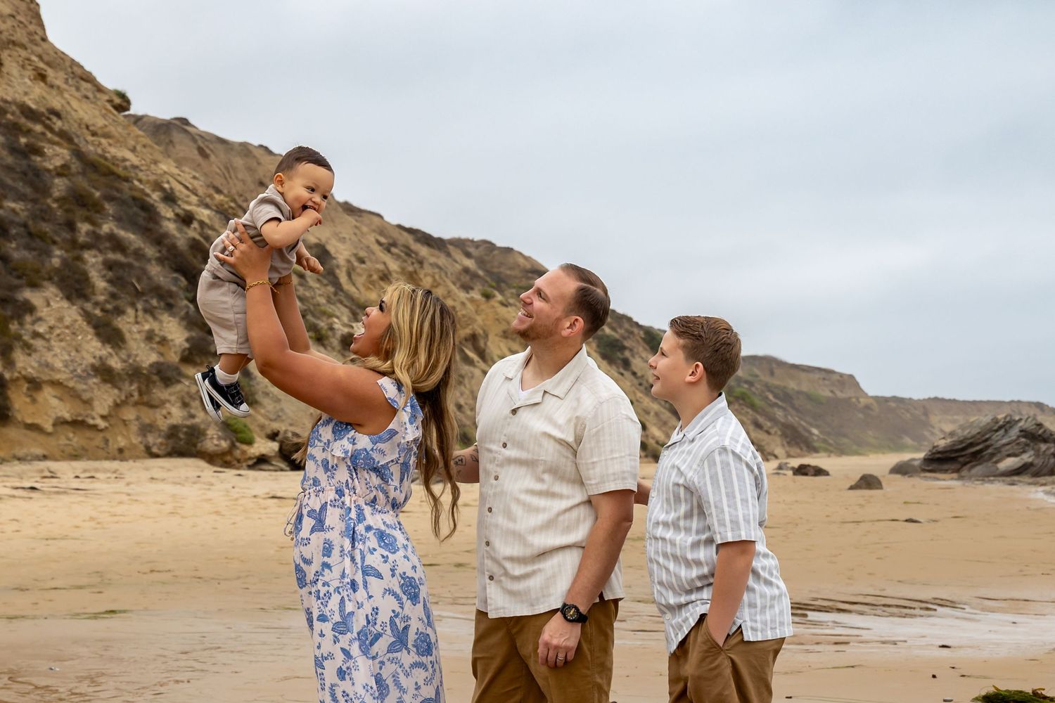 Joyful family moment captured on a sandy beach with cliffs in the background.