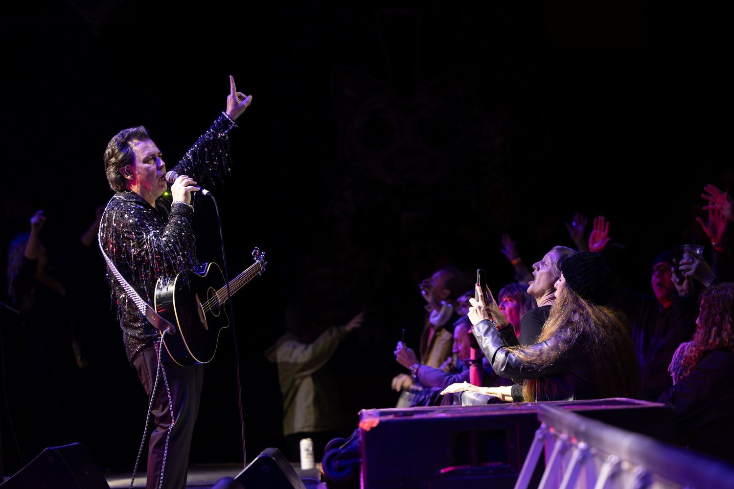 Concert performer with guitar entertaining audience in dark venue with dramatic lighting in Garden Grove.