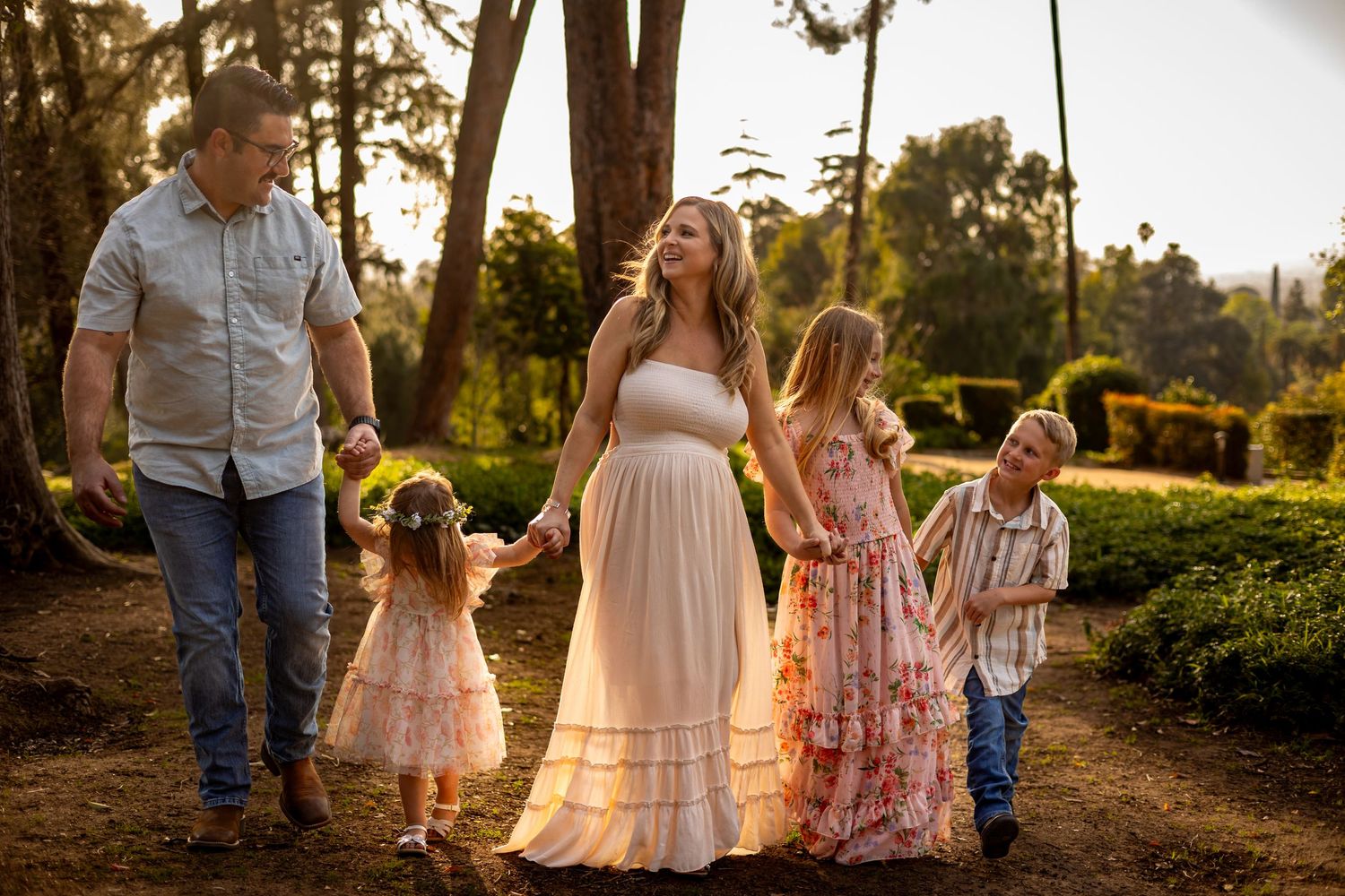 Family walking together at sunset through a wooded park in flowing dresses In Redlands.