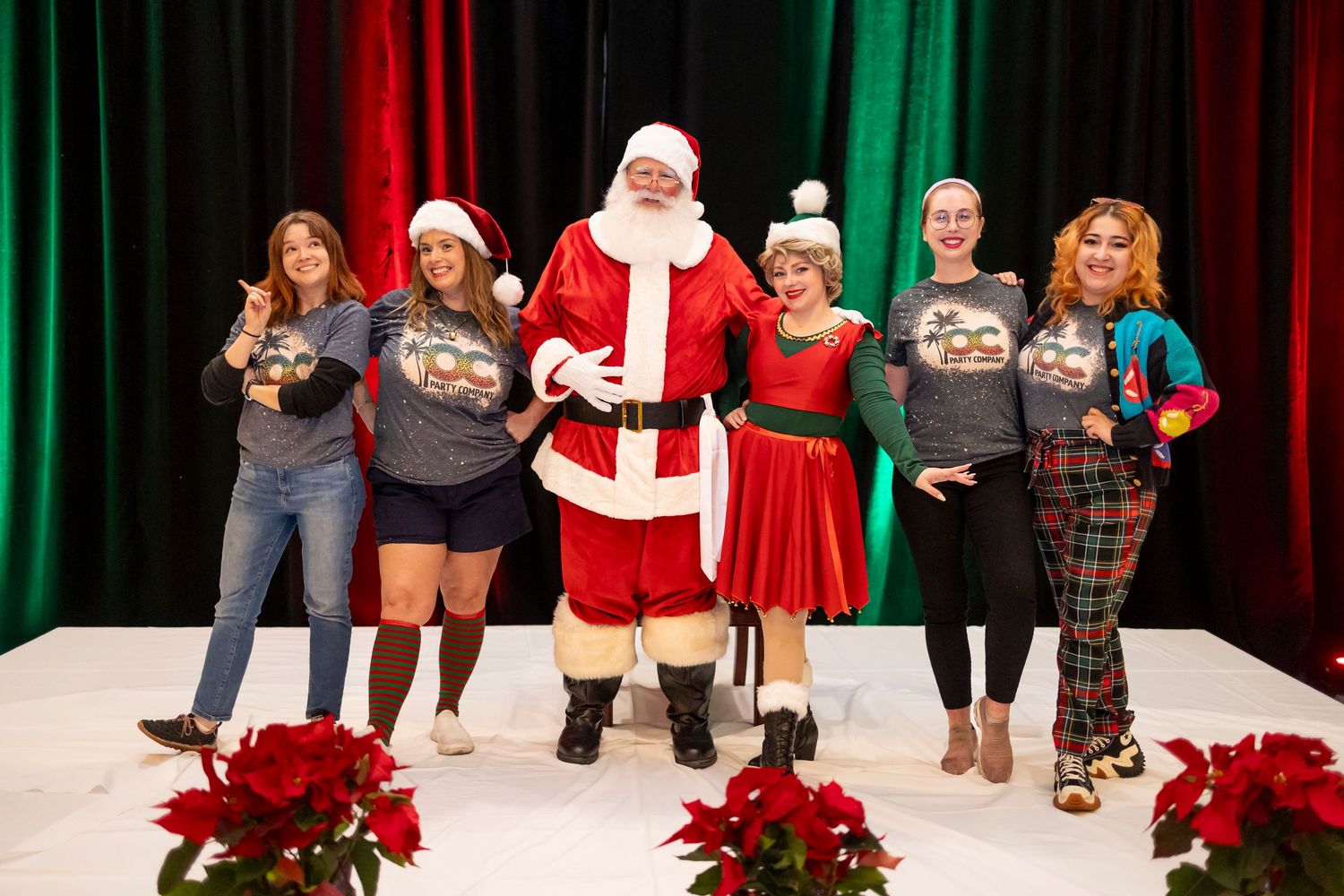 A Christmas stage show featuring Santa Claus and performers with festive red and green decorations in the background.
