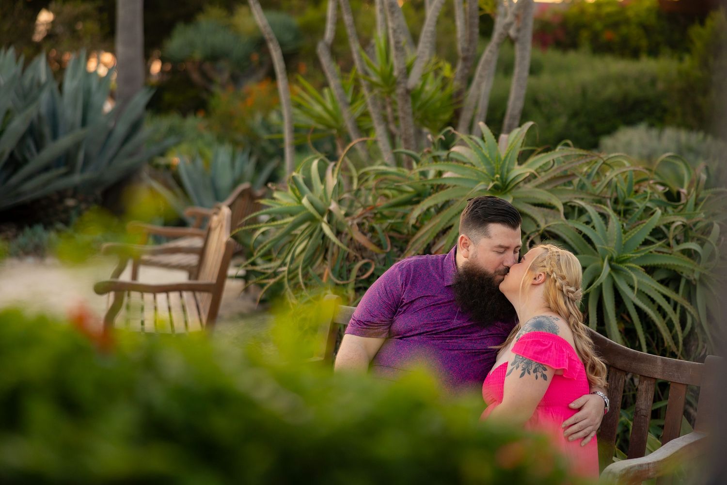 A couple embraces in a lush garden setting with tropical plants and natural lighting.