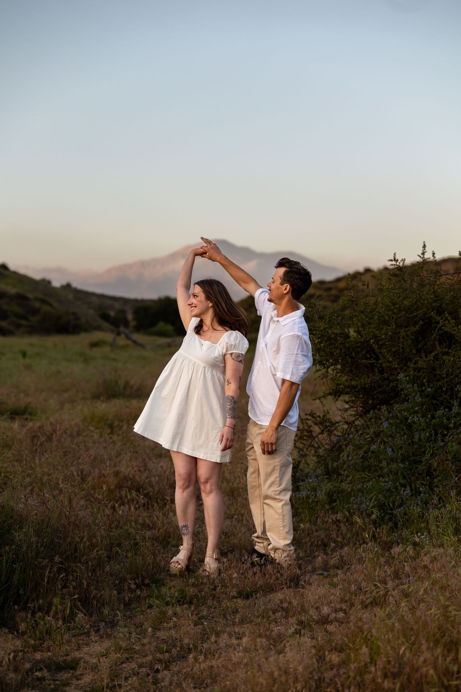 A couple dancing outdoors with mountains in the background during sunset.