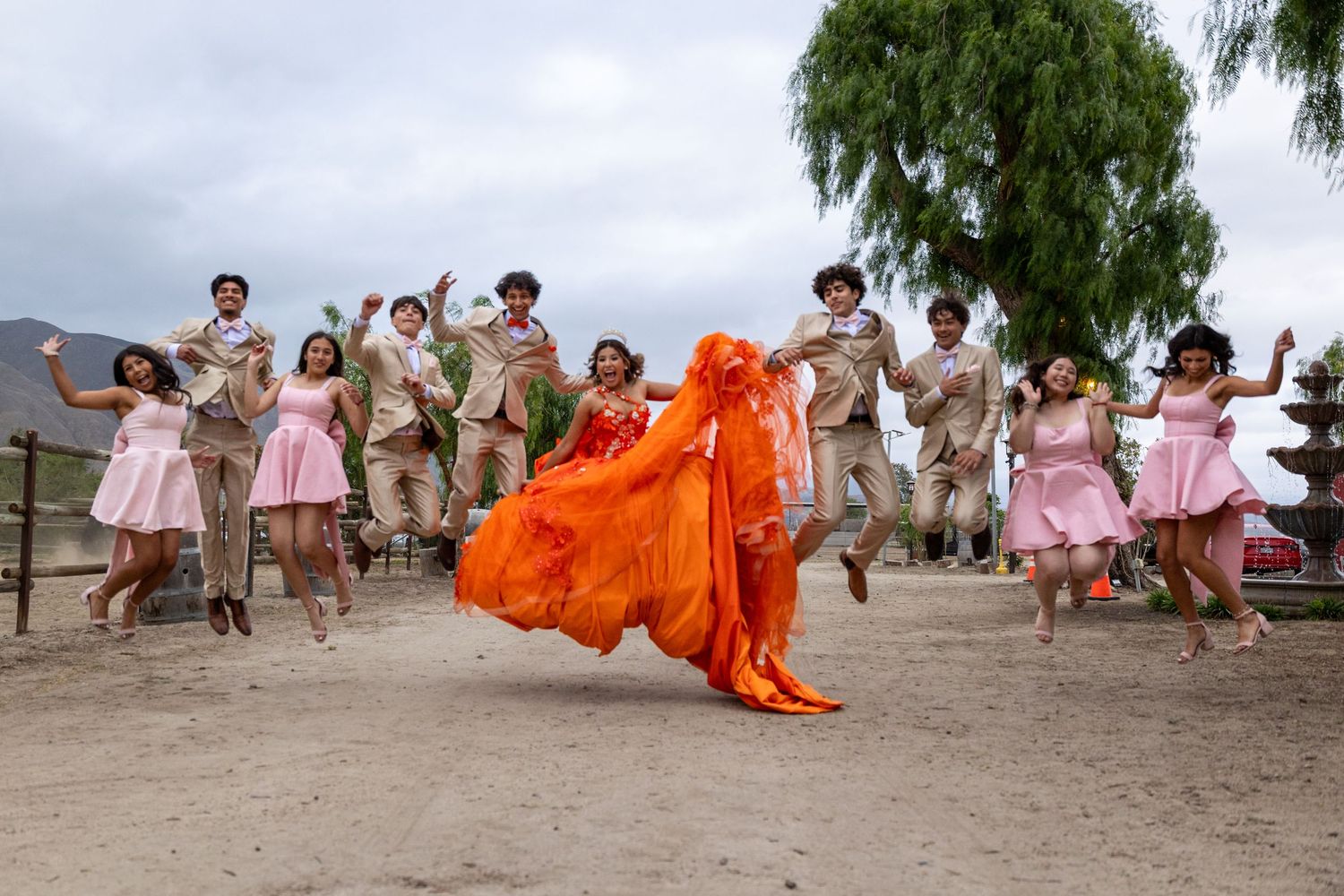 A celebratory group jumping photo with orange and pink attire against a desert landscape.