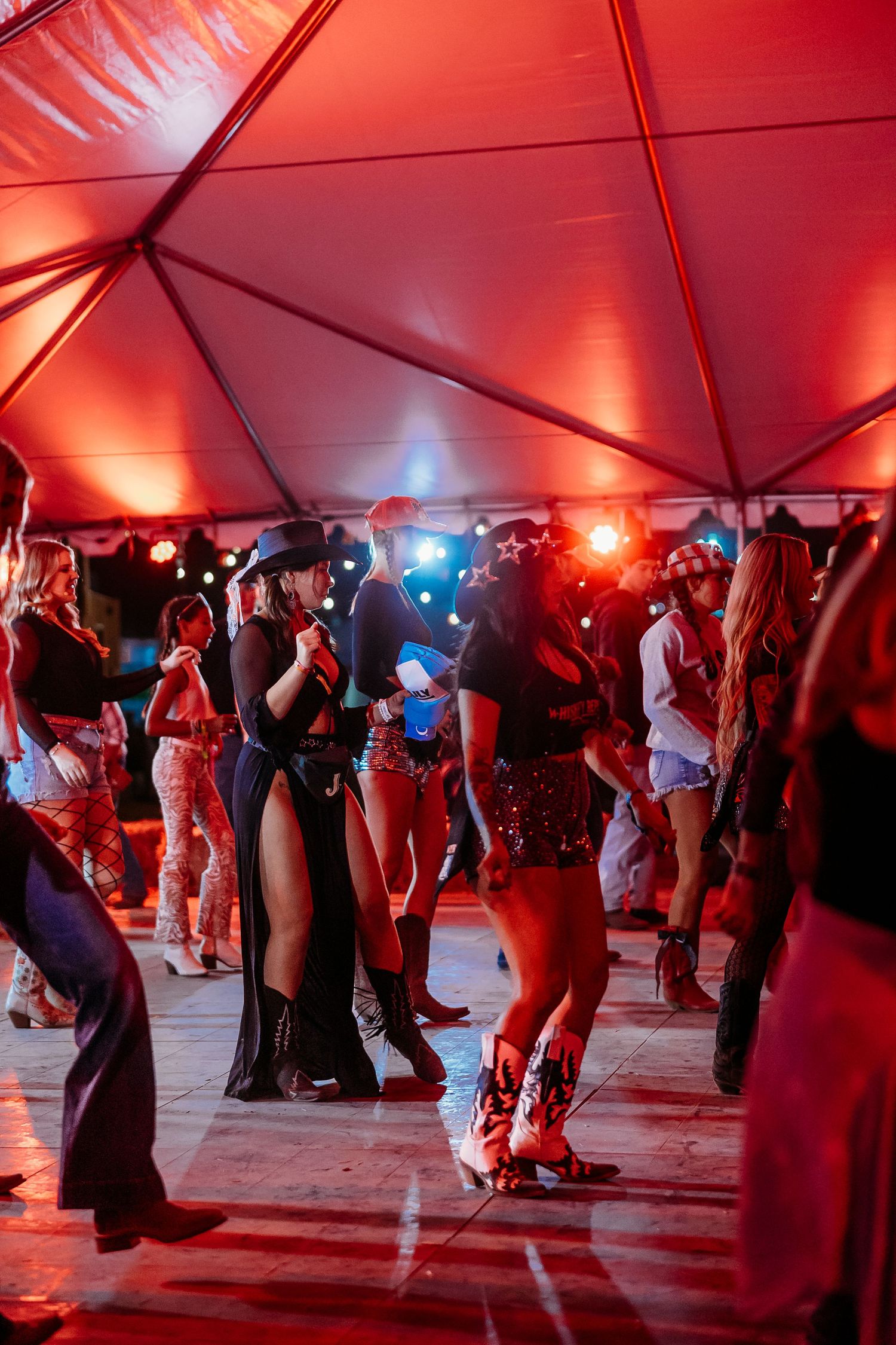 Dancers moving across a dance floor under dramatic red tent lighting at an outdoor event.