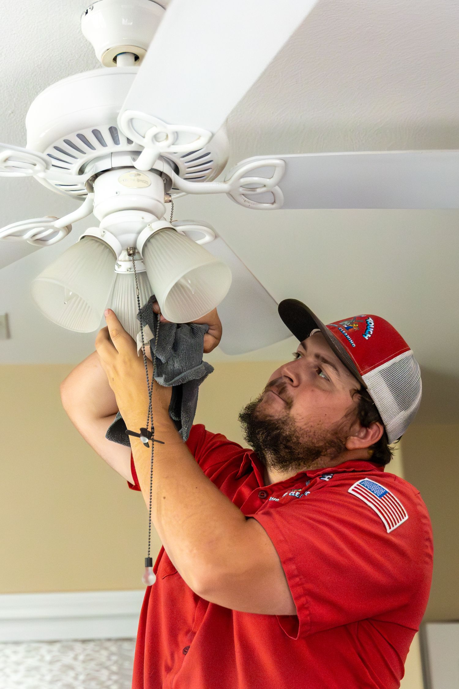 Electrician in red uniform and cap installing white ceiling fan in sequence of installation steps.