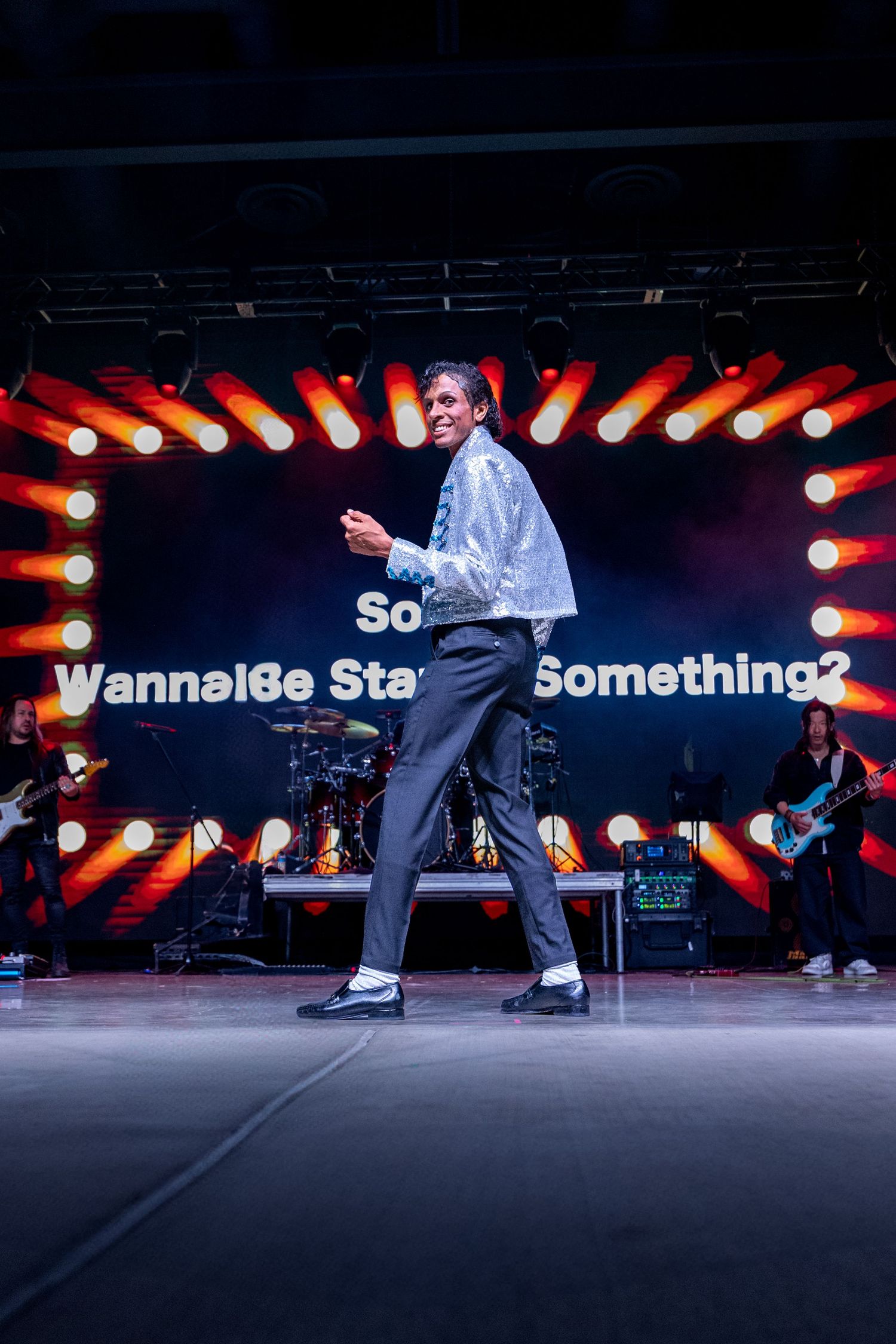 Performer on stage with dramatic red lighting and text display in background.