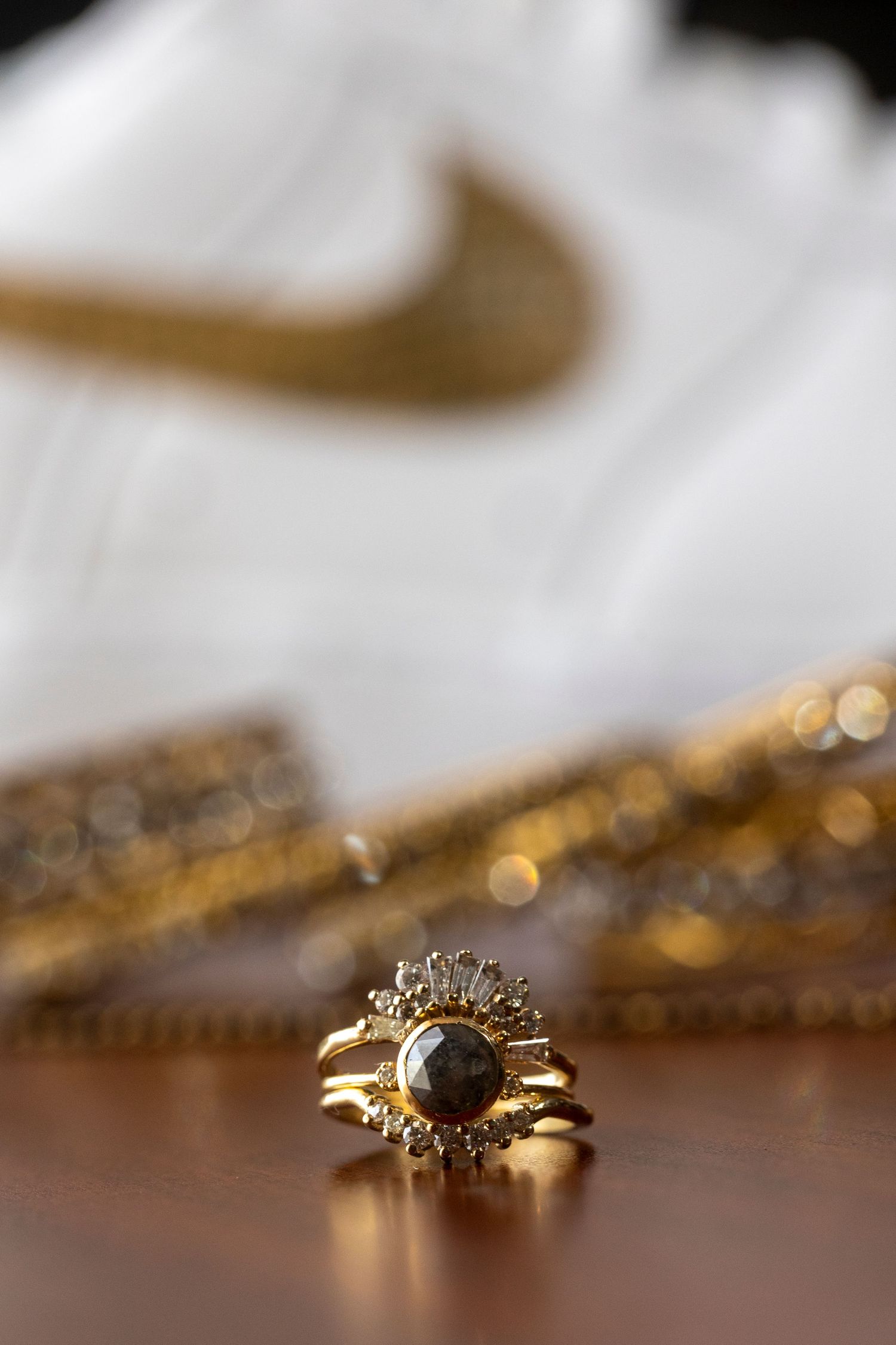 Close-up of an ornate gold engagement ring with diamonds on a reflective wooden surface.