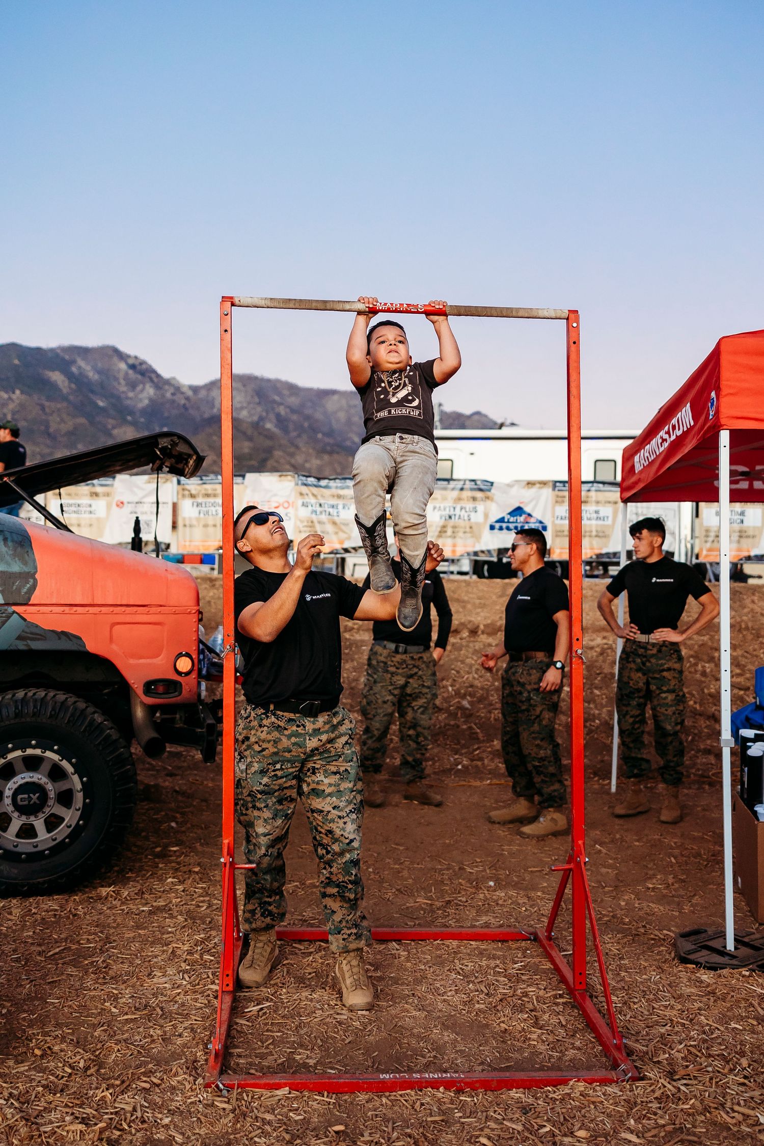 People gather around a red pull-up bar frame at an outdoor event.