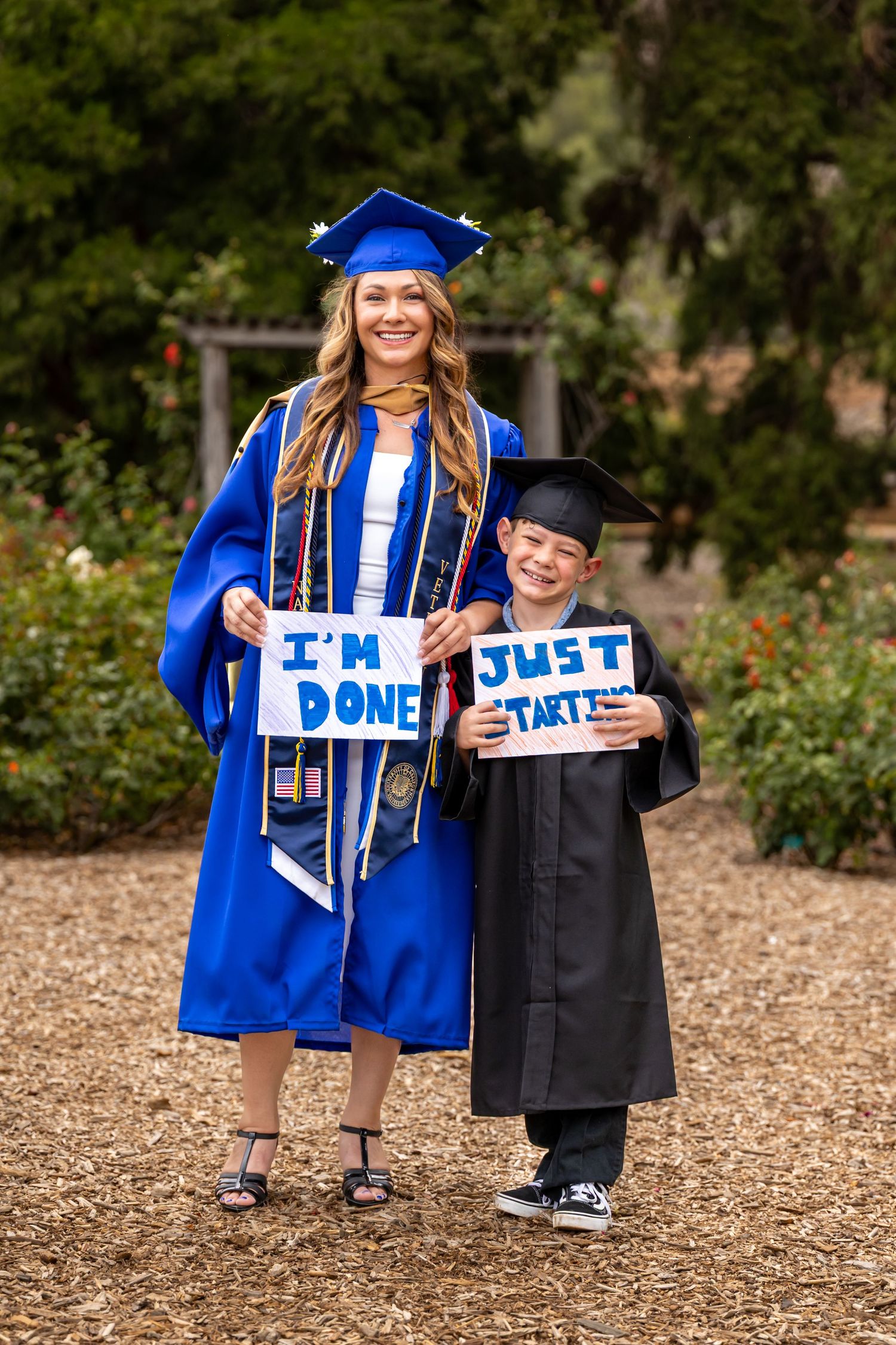 Graduate in blue regalia holding 'DONE' sign while posing with her son in Riverside.
