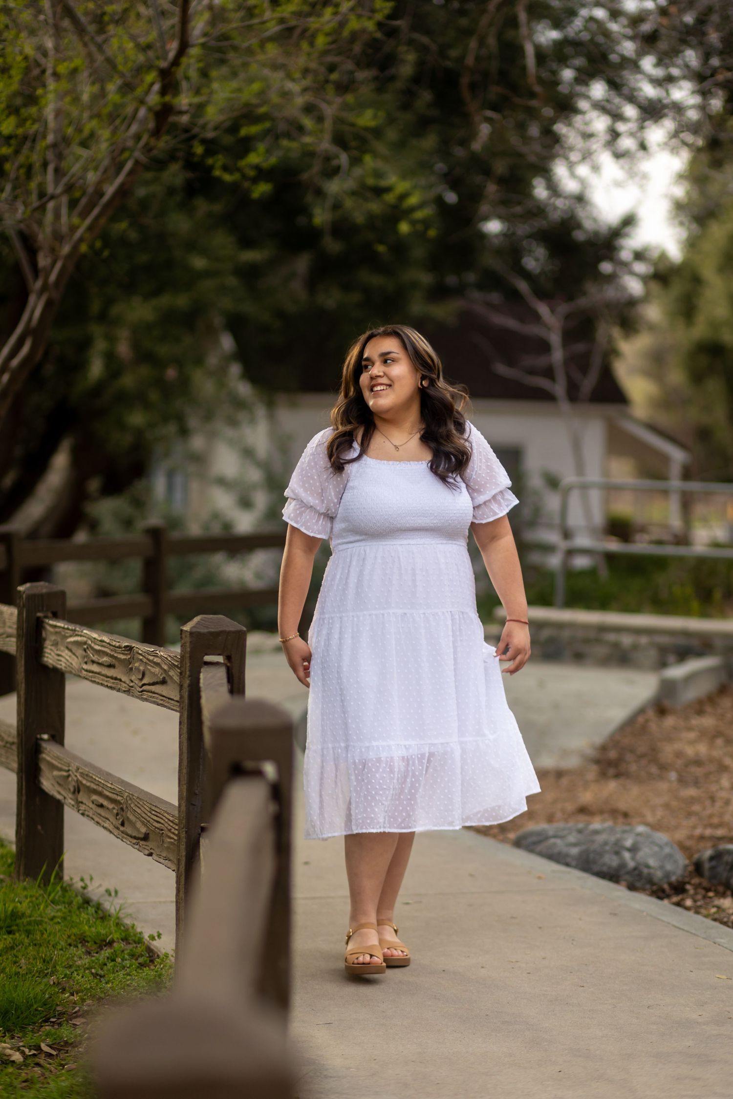 A woman in a white summer dress walks along a path surrounded by greenery in Oak Glen.