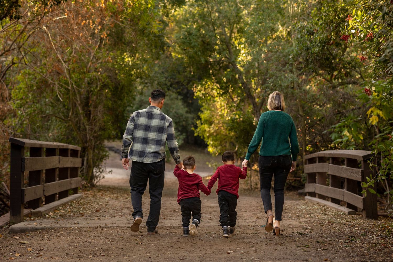 Family walks together on wooden bridge path through autumn foliage in park setting.